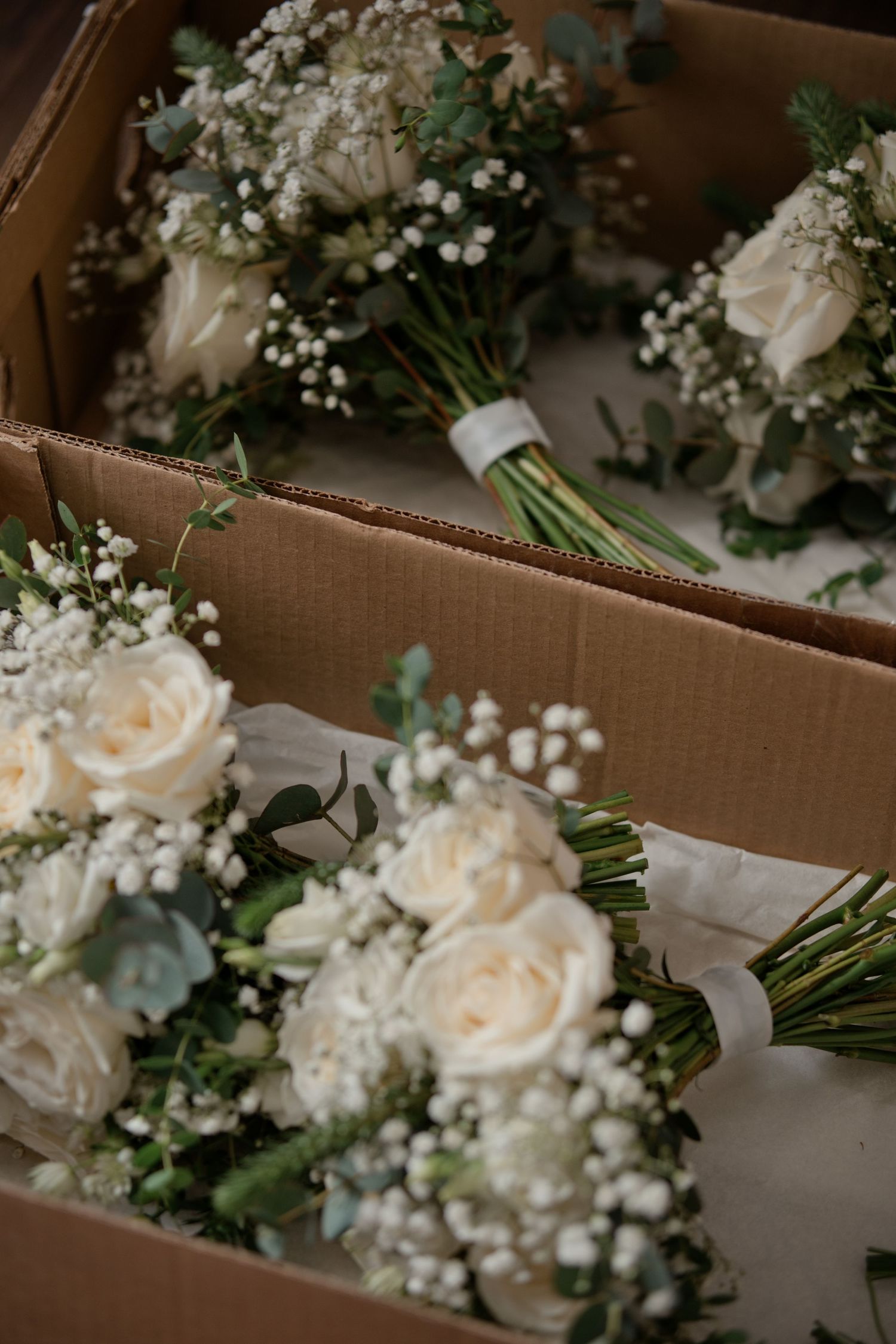 Multiple white rose and baby's breath wedding bouquets arranged in a cardboard delivery box.