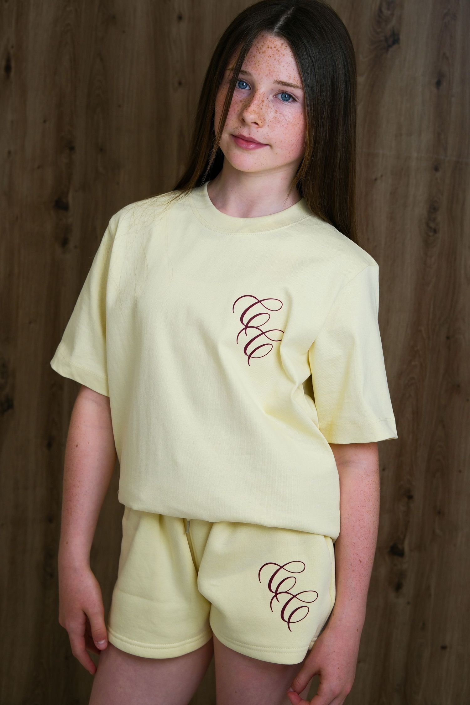 Girl wearing yellow matching shorts and t-shirt set with embroidered monogram logo design.