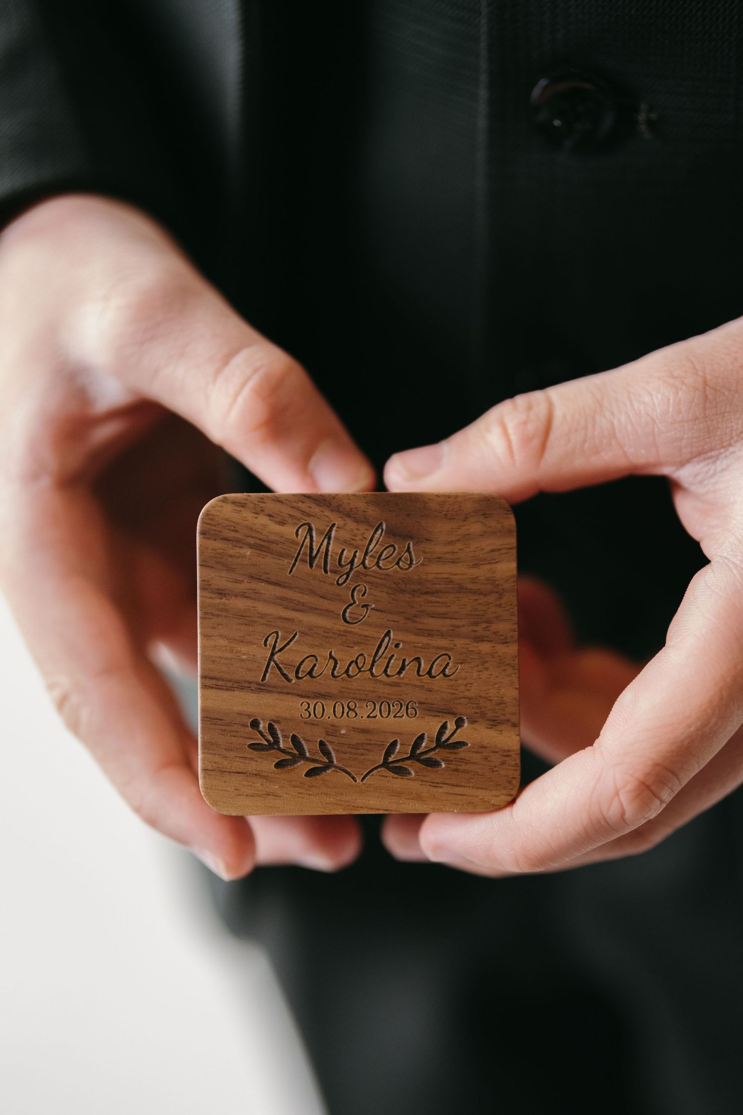 Hands holding a personalized wooden ring box engraved with Myles and Karolina 30.08.2020.
