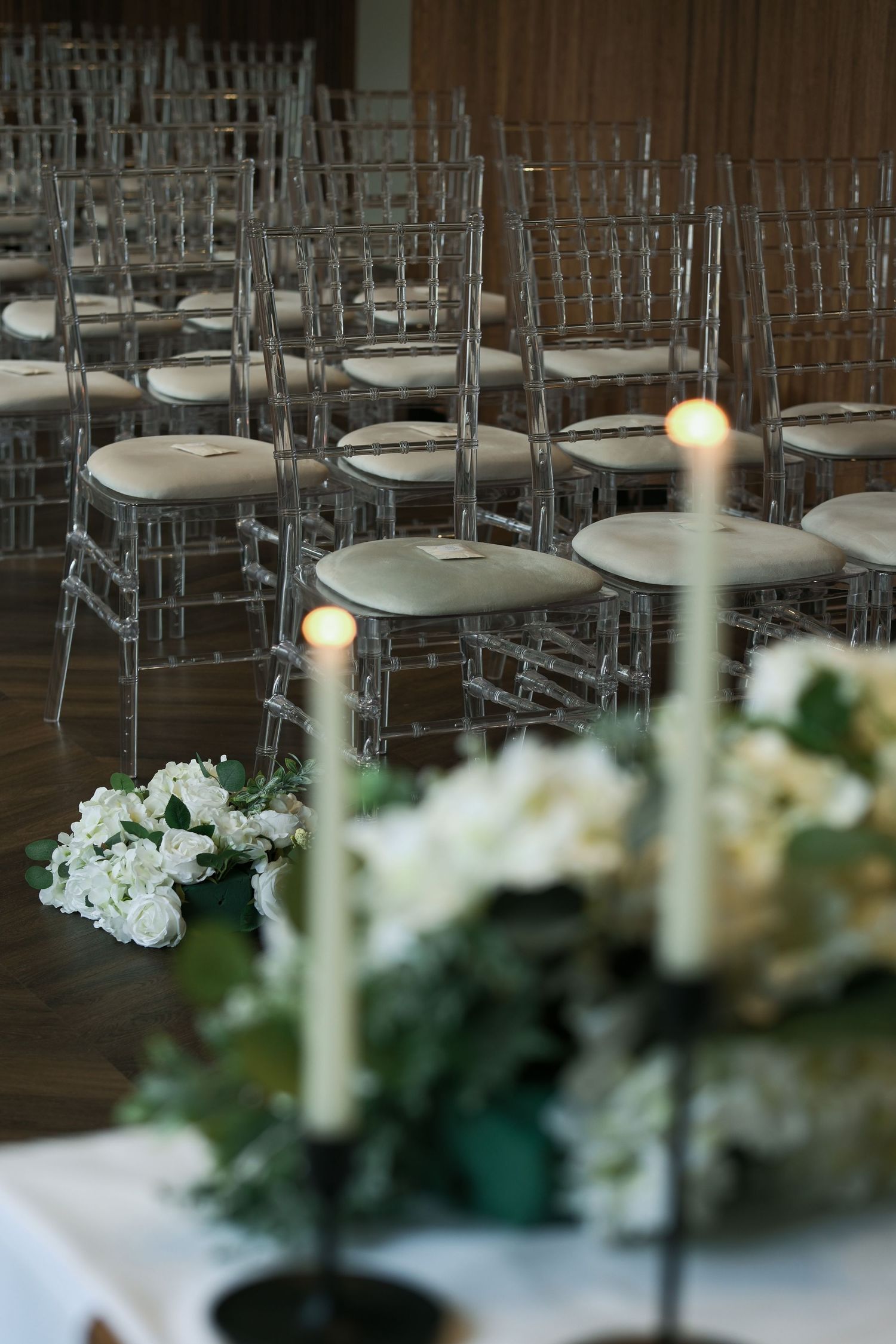Elegant wedding ceremony venue with ghost chairs, white floral arrangements, and lit taper candles.