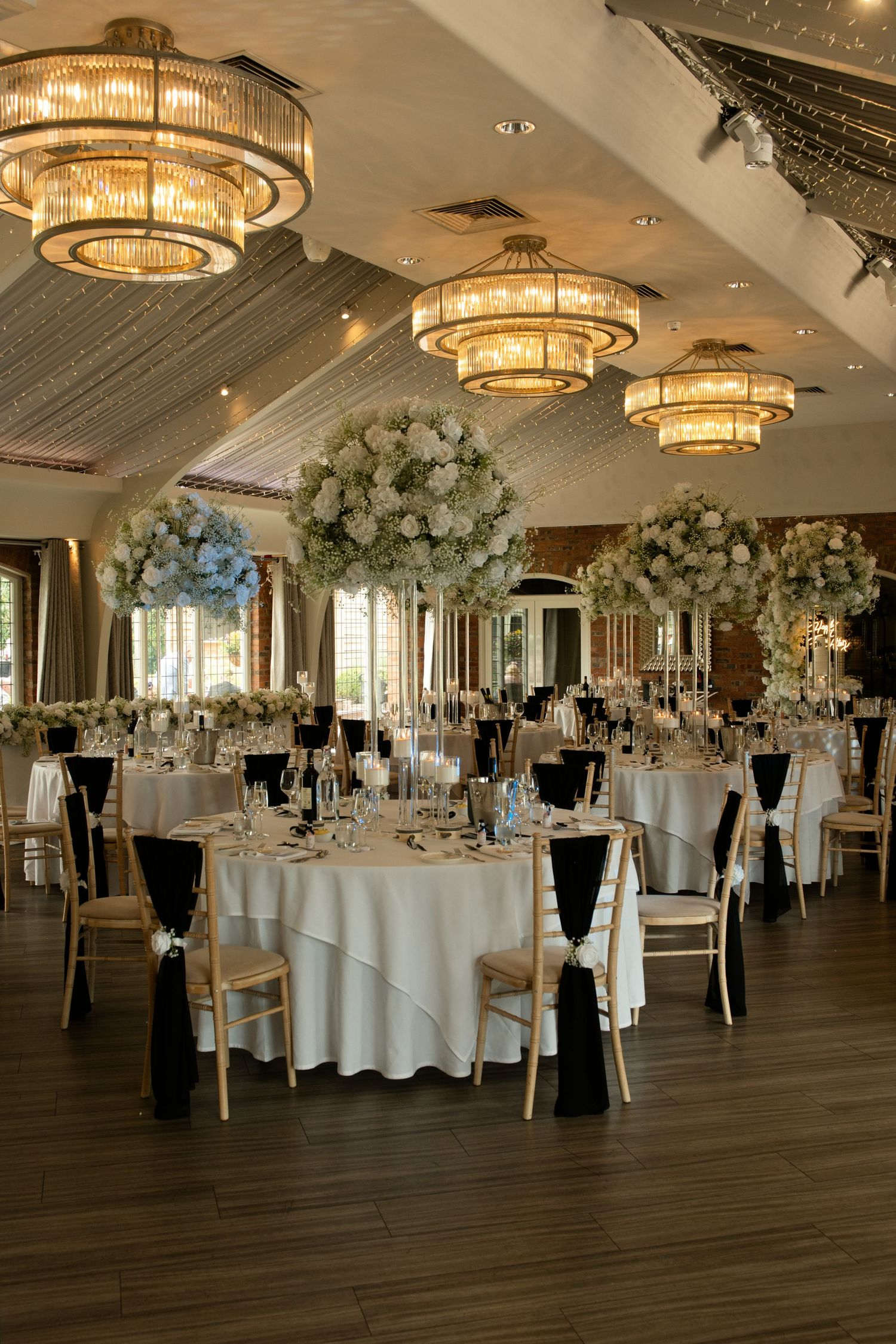 Elegant wedding reception hall with tall floral centerpieces and gold chandeliers.