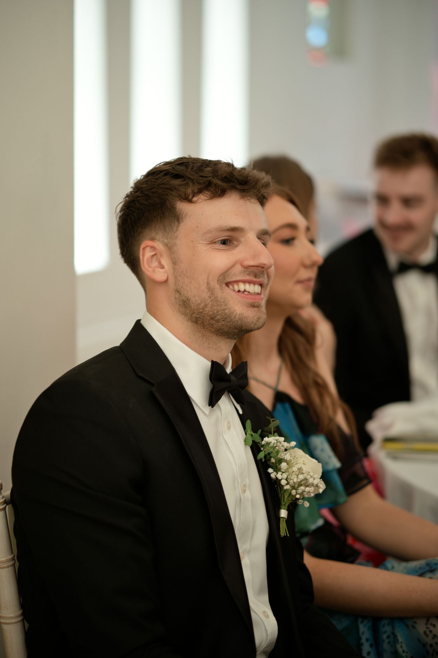 Smiling groom in black tuxedo with boutonniere at wedding ceremony.