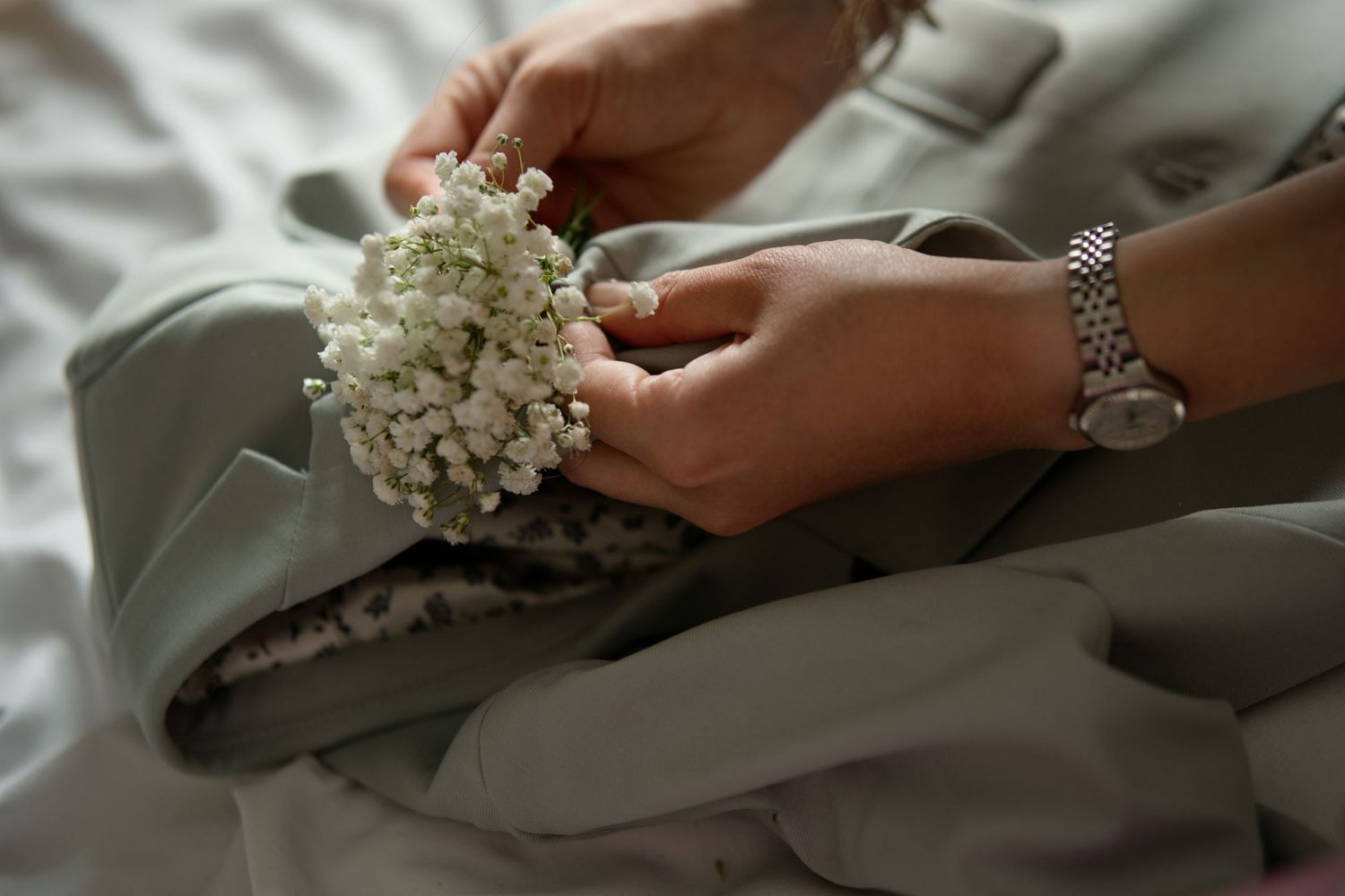 Hands arranging white baby's breath flowers on sage green bridesmaid dress with silver watch.