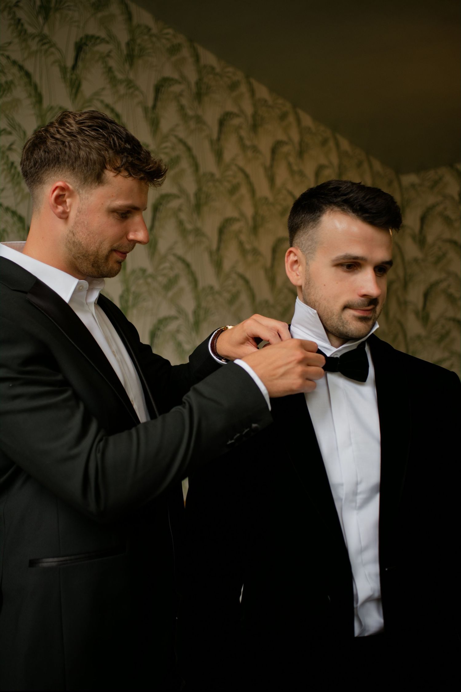 Best man helping groom adjust bow tie while getting ready for wedding ceremony.