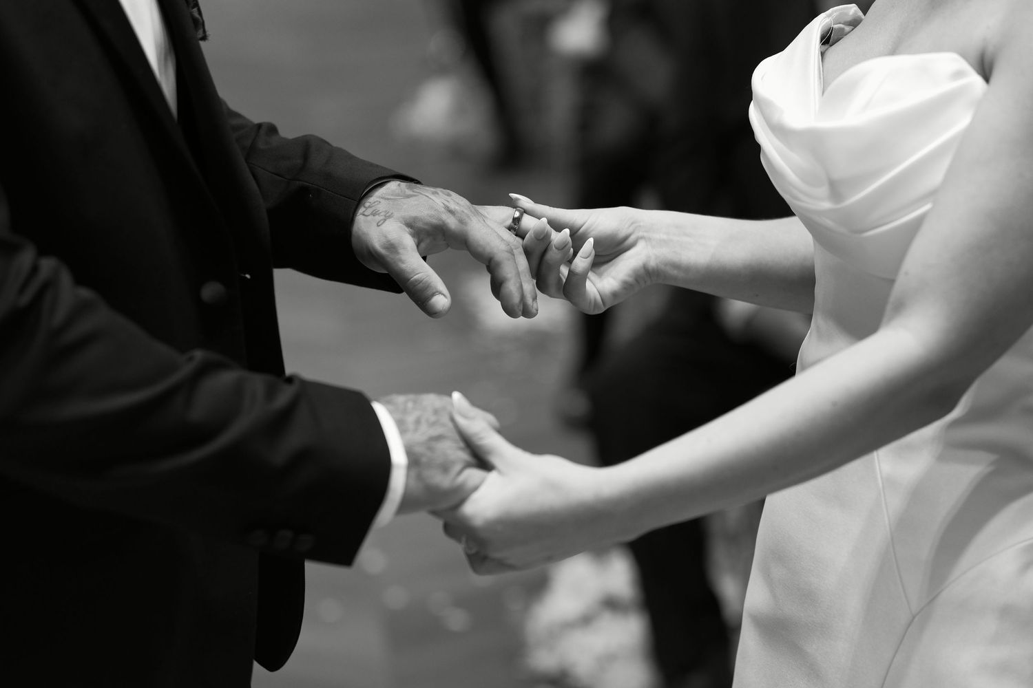 Groom placing wedding ring on bride's finger during ceremony in black and white photo.