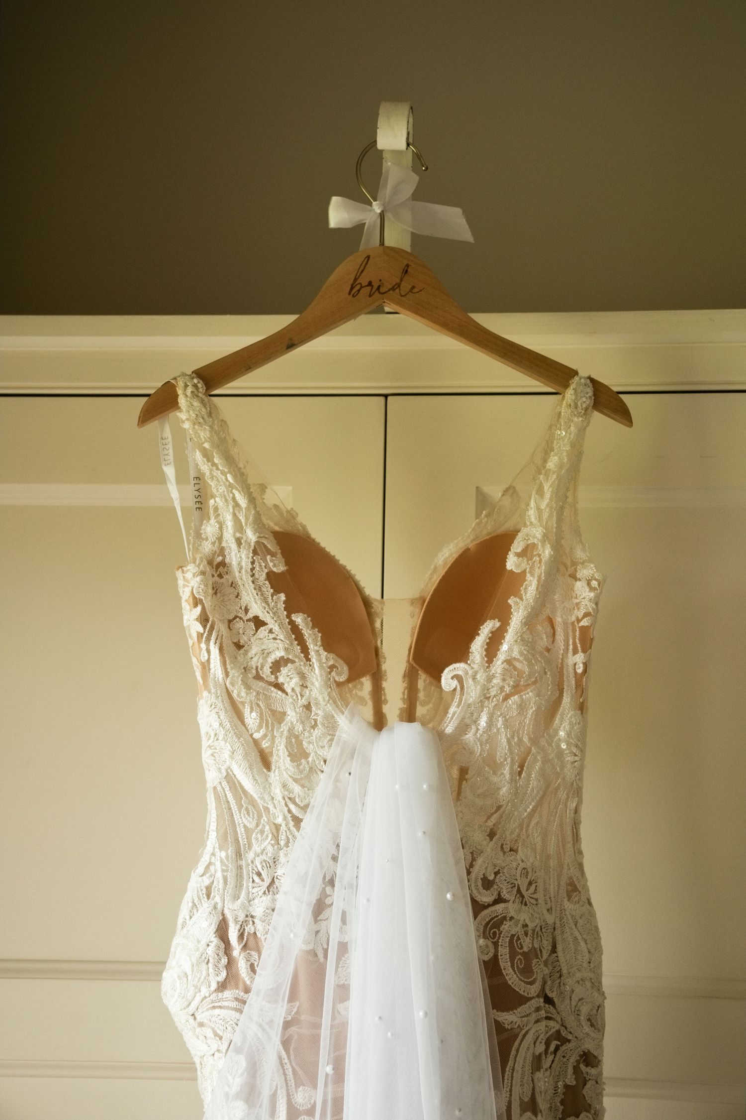 Intricate lace wedding gown hanging on wooden bride hanger.