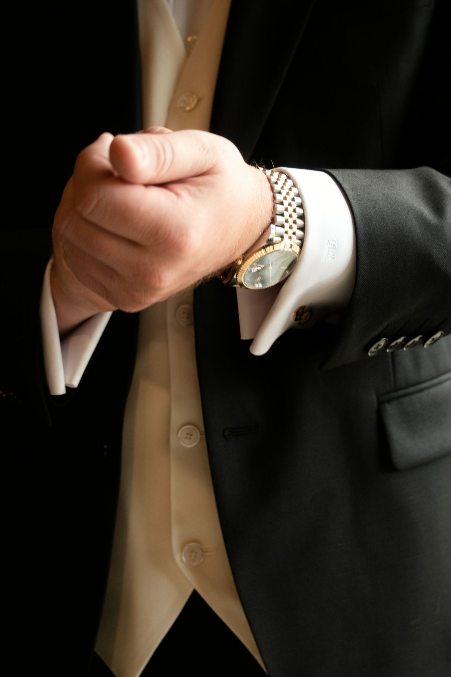 Close-up of groom adjusting suit jacket sleeve revealing gold Rolex watch and cream waistcoat.