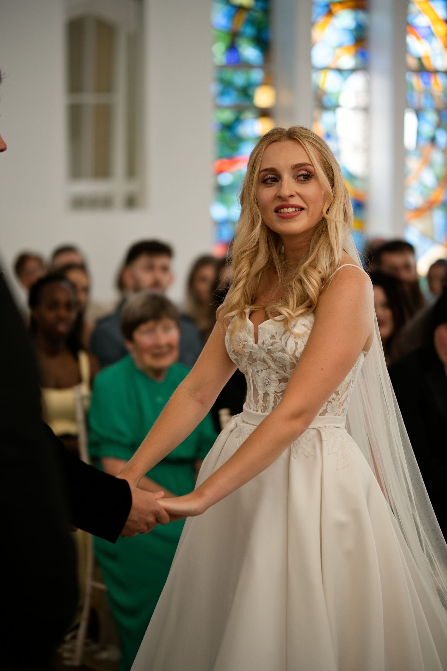 Smiling blonde bride in lace wedding gown holding hands at church altar ceremony.