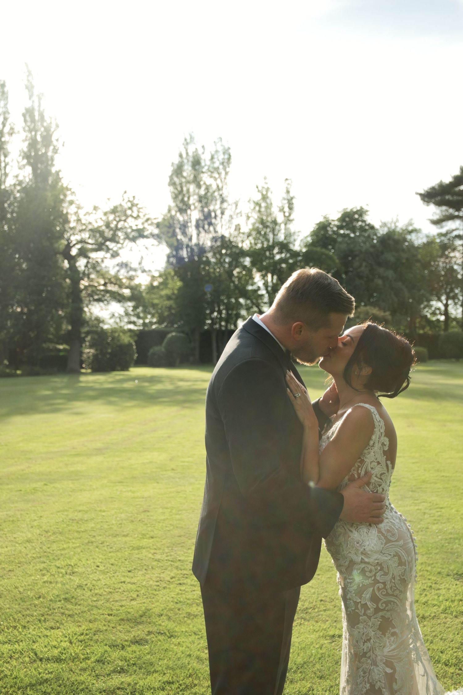 Bride and groom sharing a kiss on sunlit green lawn at outdoor wedding.