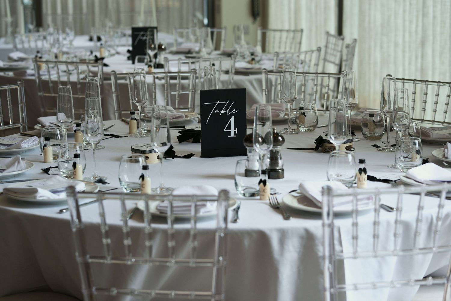 Elegant wedding reception tables set with white linens, crystal glasses, and a Table 4 sign.