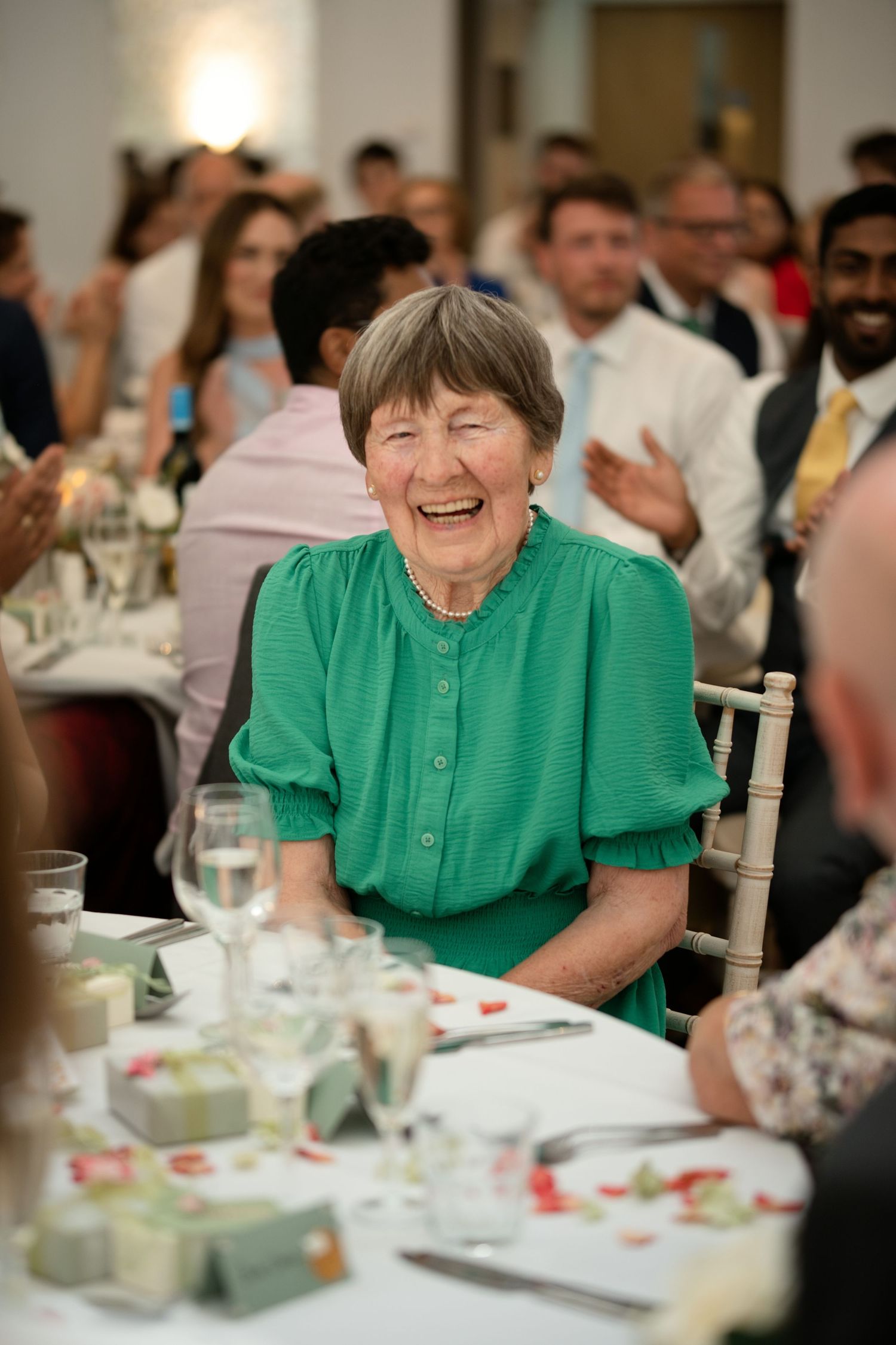 Elderly woman in green dress laughing joyfully at a wedding reception dinner.