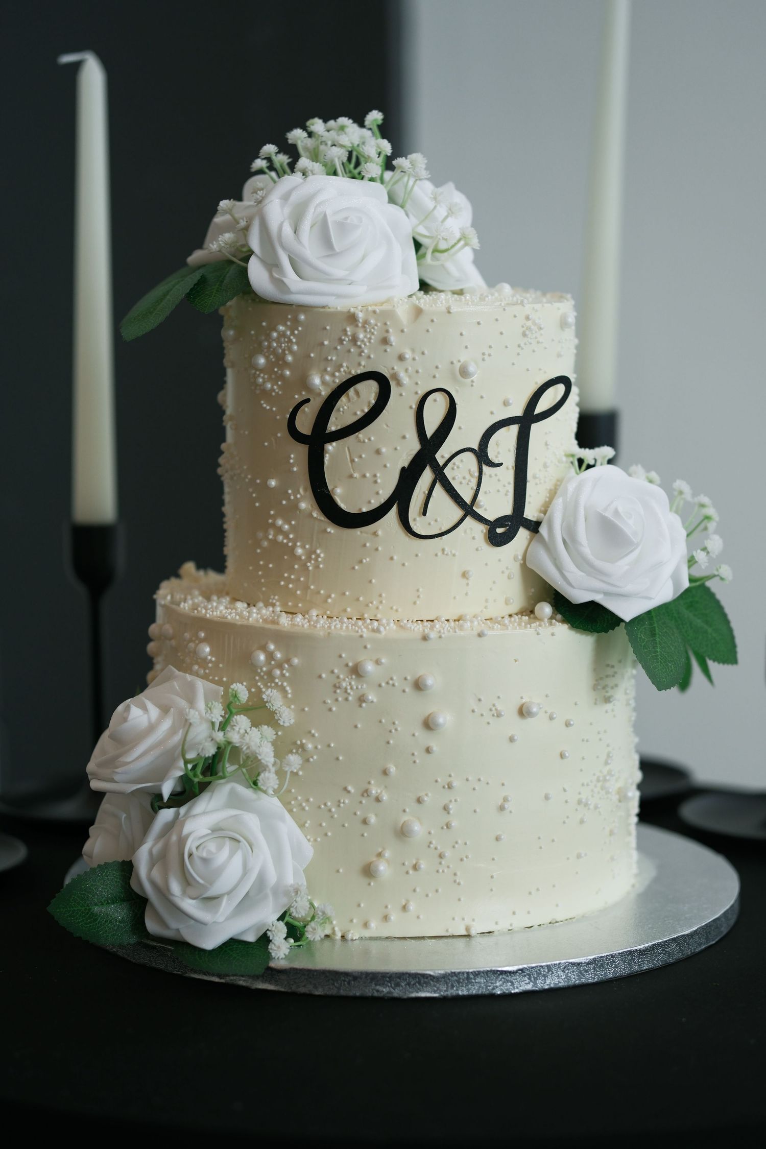 Elegant two-tier white wedding cake with roses and C&L monogram topper.