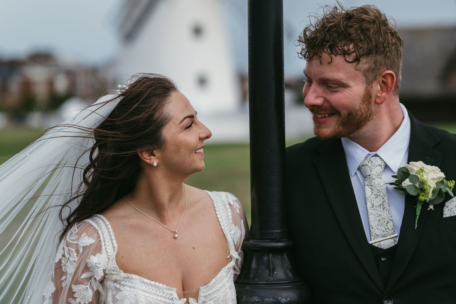 A bride and groom share a romantic glance beside a lamppost on their wedding day outdoors.