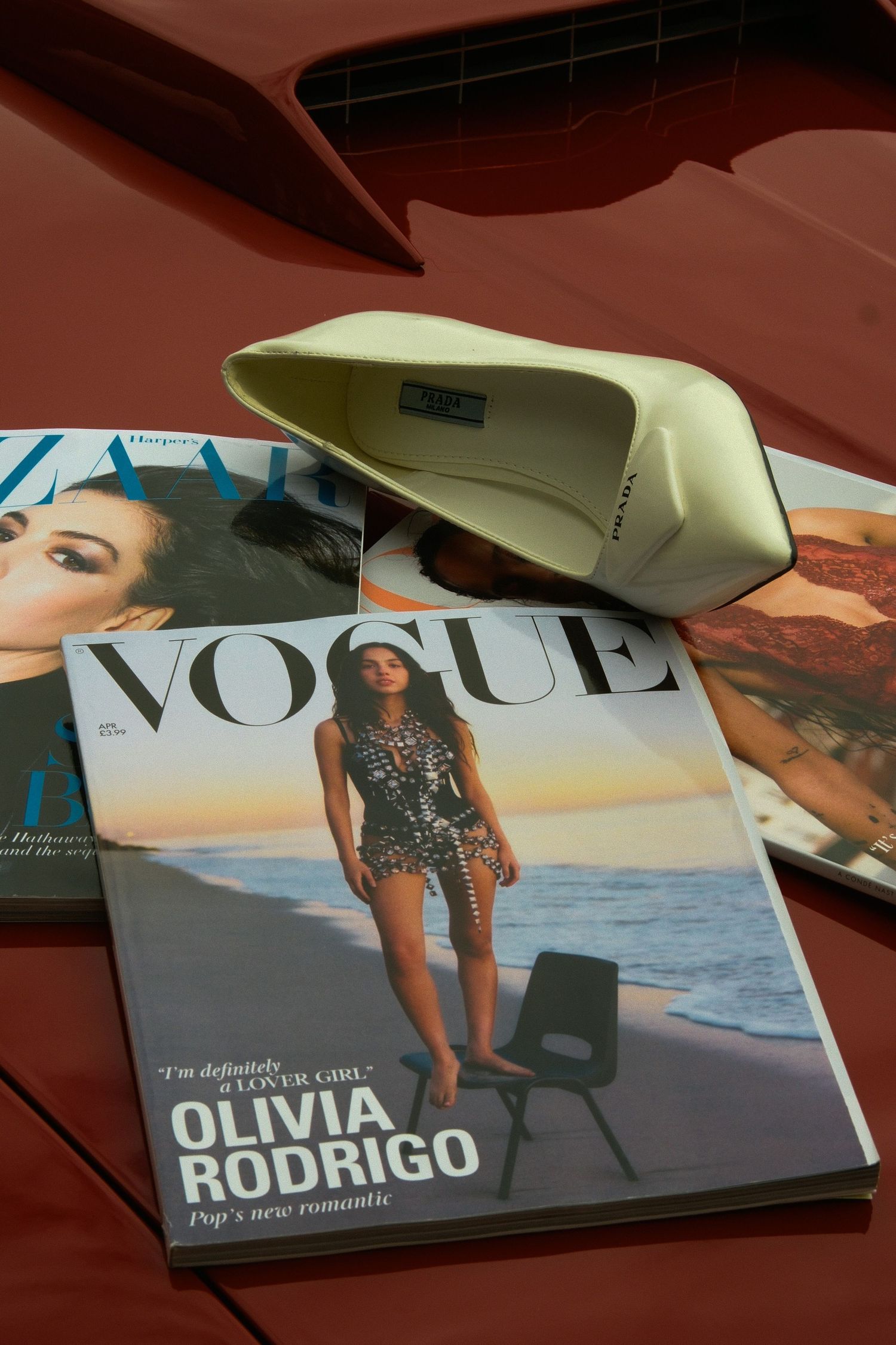 Vogue magazine featuring Olivia Rodrigo cover with Harper's Bazaar and a green Prada heel on red surface.