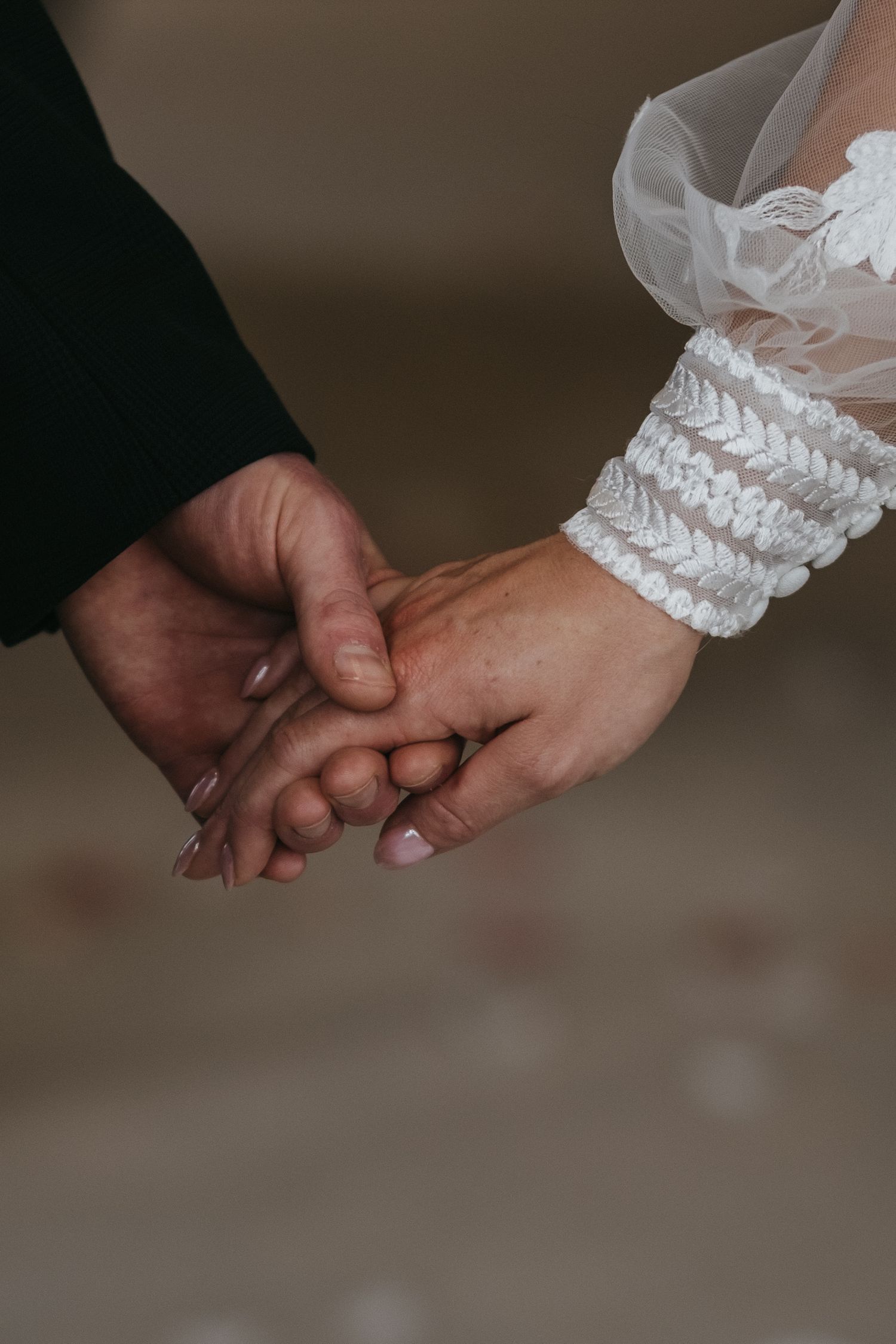 Close-up of bride and groom holding hands, bride wearing white lace wedding glove and veil.