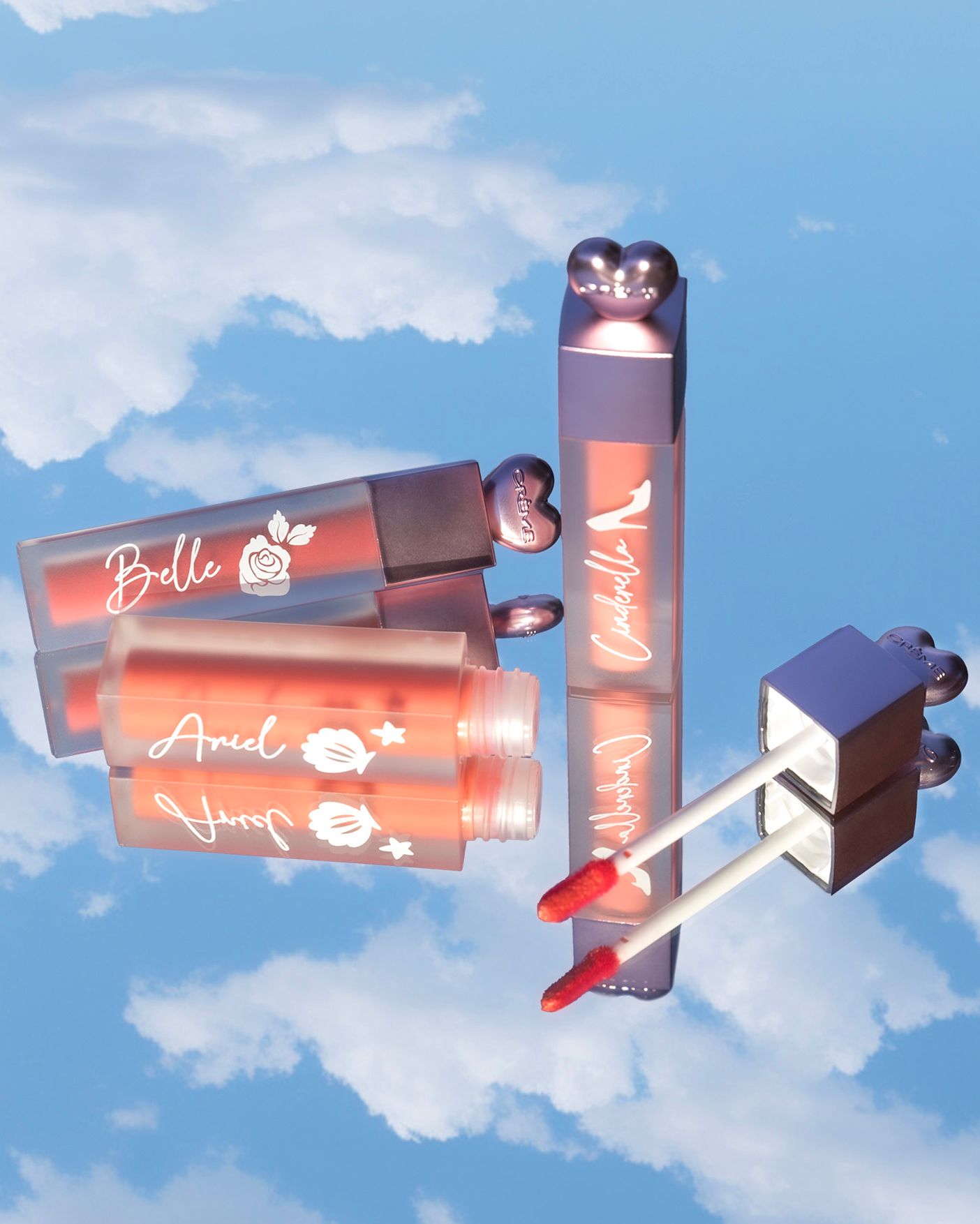 Disney Princess lip gloss set featuring Belle, Ariel, and Cinderella themed tubes floating against a dreamy blue sky.