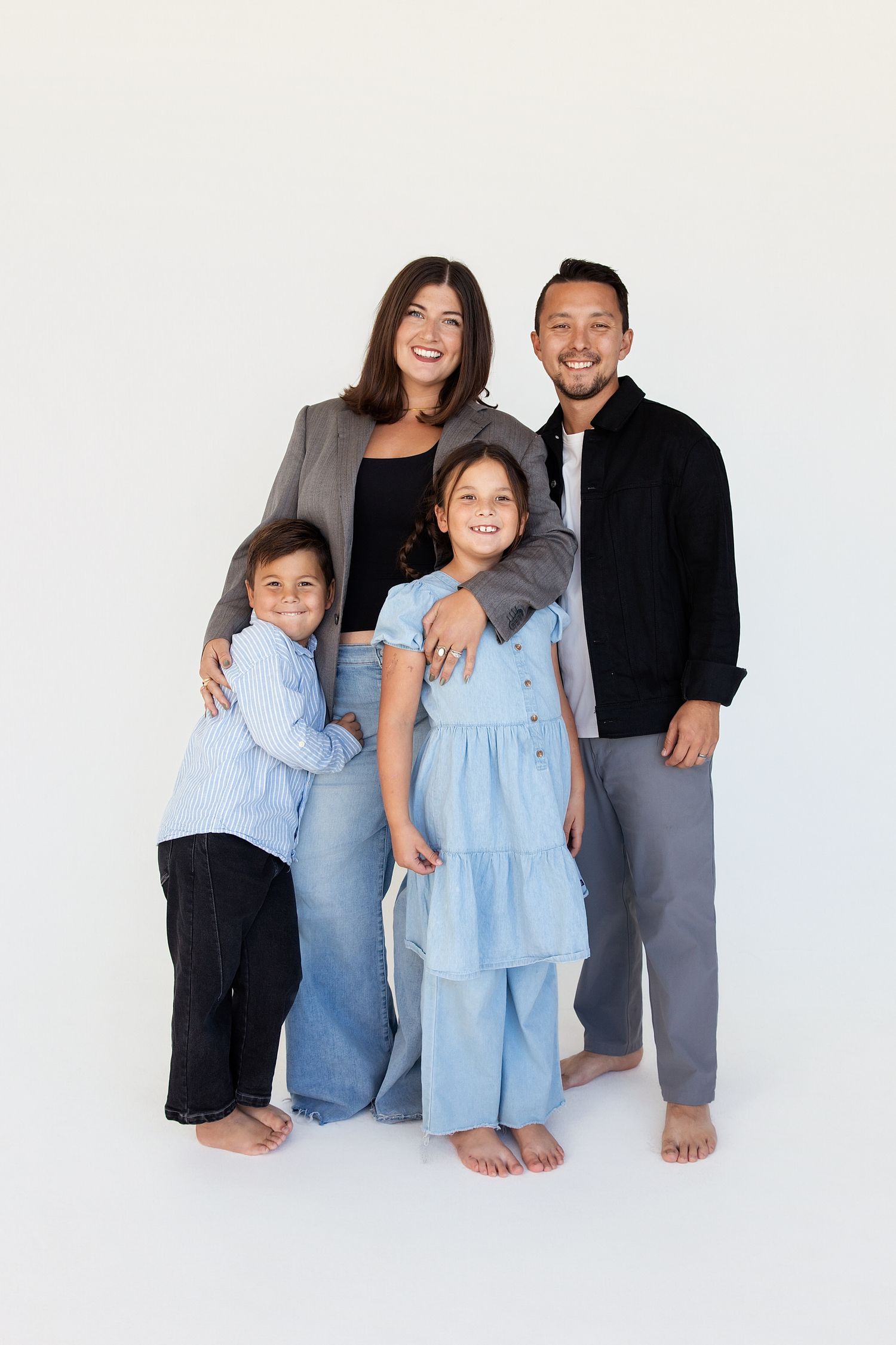 Happy family of four posing together in a bright studio, wearing casual blue and black outfits, smiling warmly.