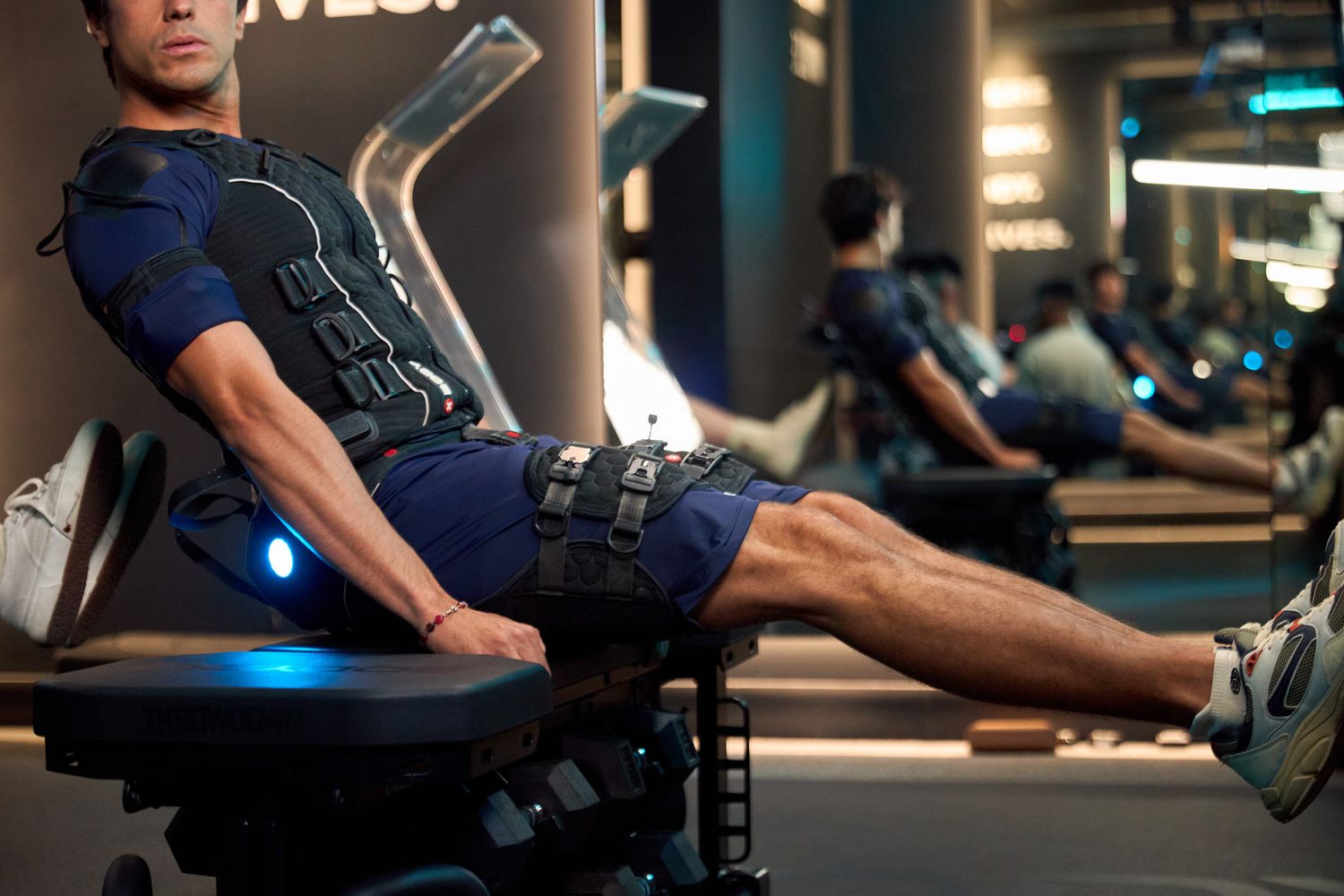 Man wearing EMS training suit performing leg exercises on a machine in a modern fitness studio.