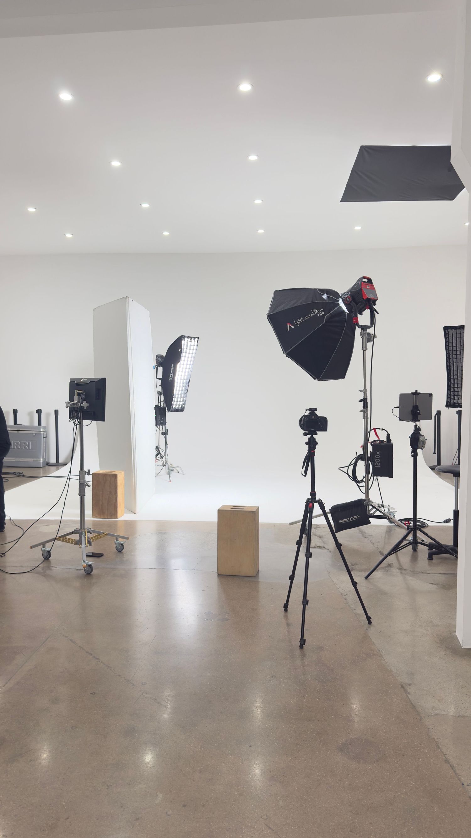A professional photography studio with multiple light stands, softboxes, and equipment on a white backdrop.
