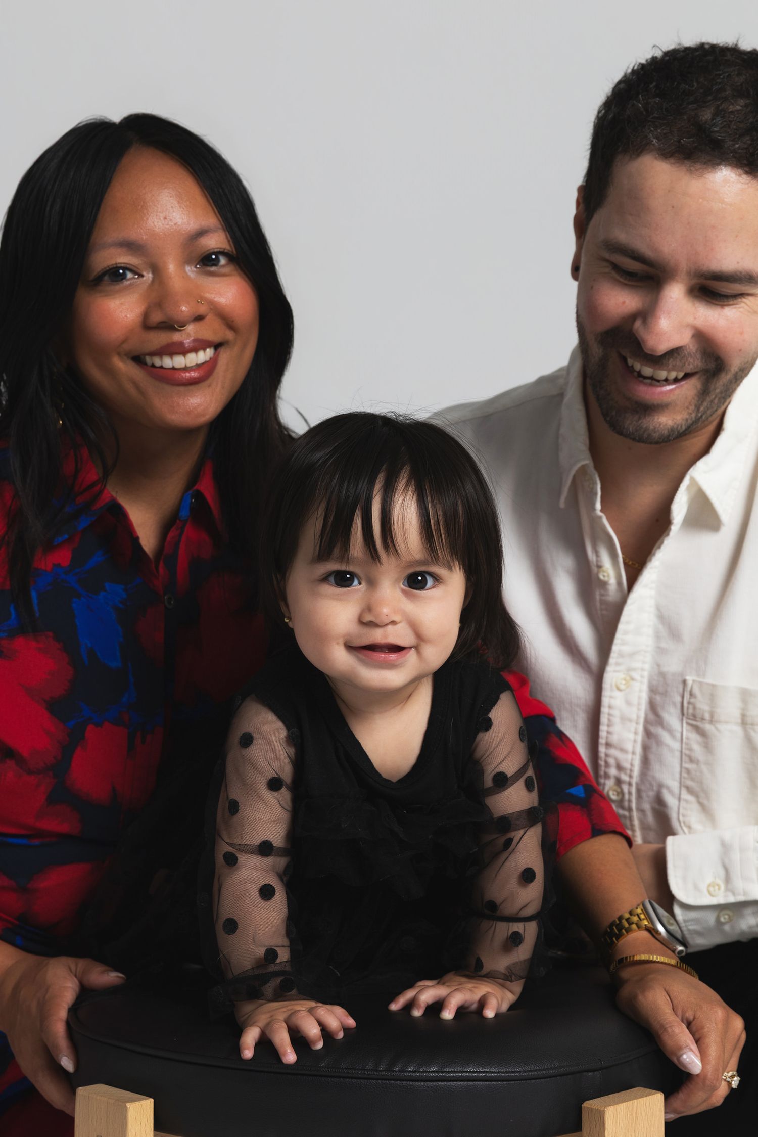A smiling family portrait with a mother, father, and baby girl in a studio setting.