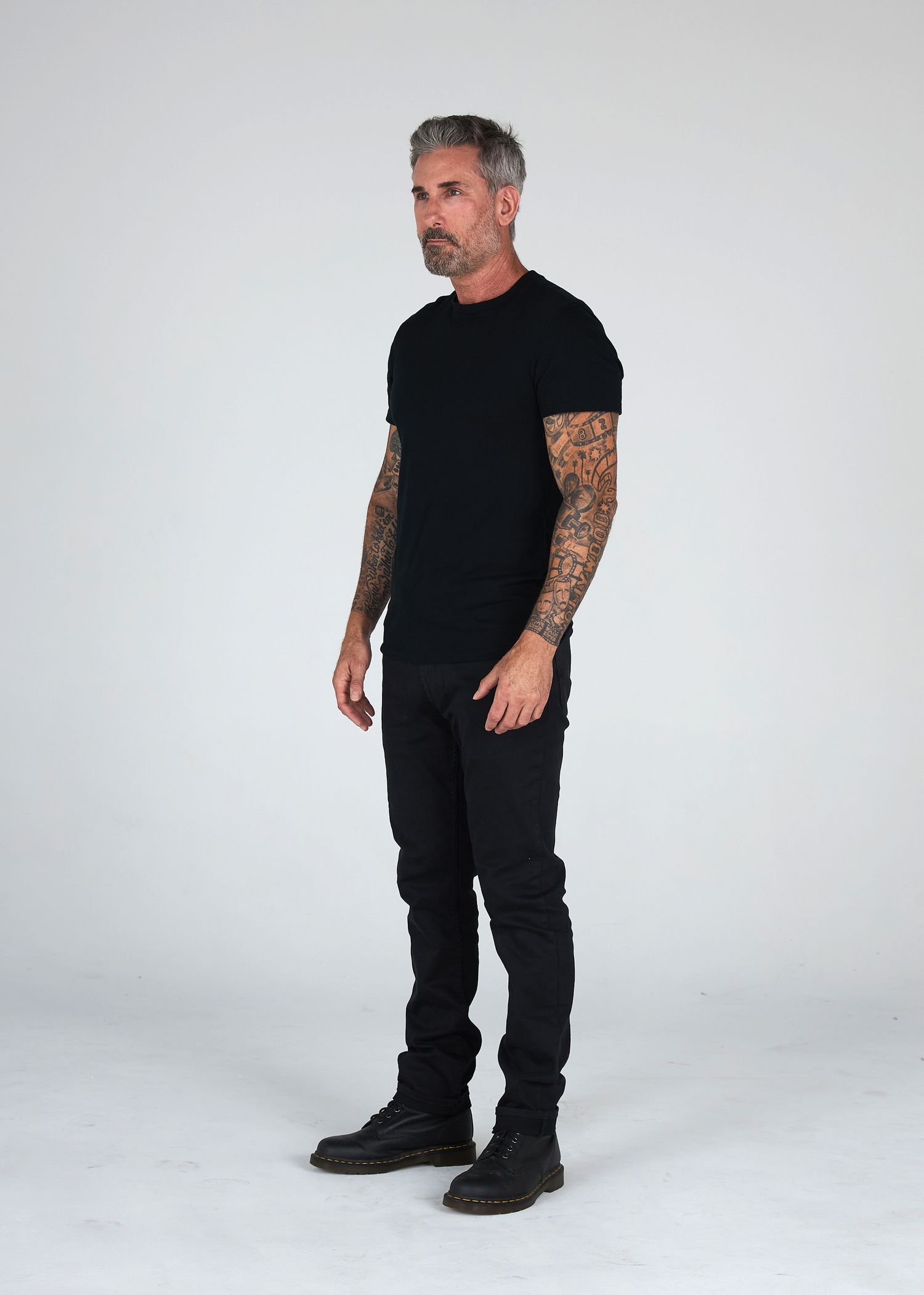 Full-length model digital session photo wearing a form-fitting black t-shirt and black jean jeans against a plain white wall, by Belva Chan.