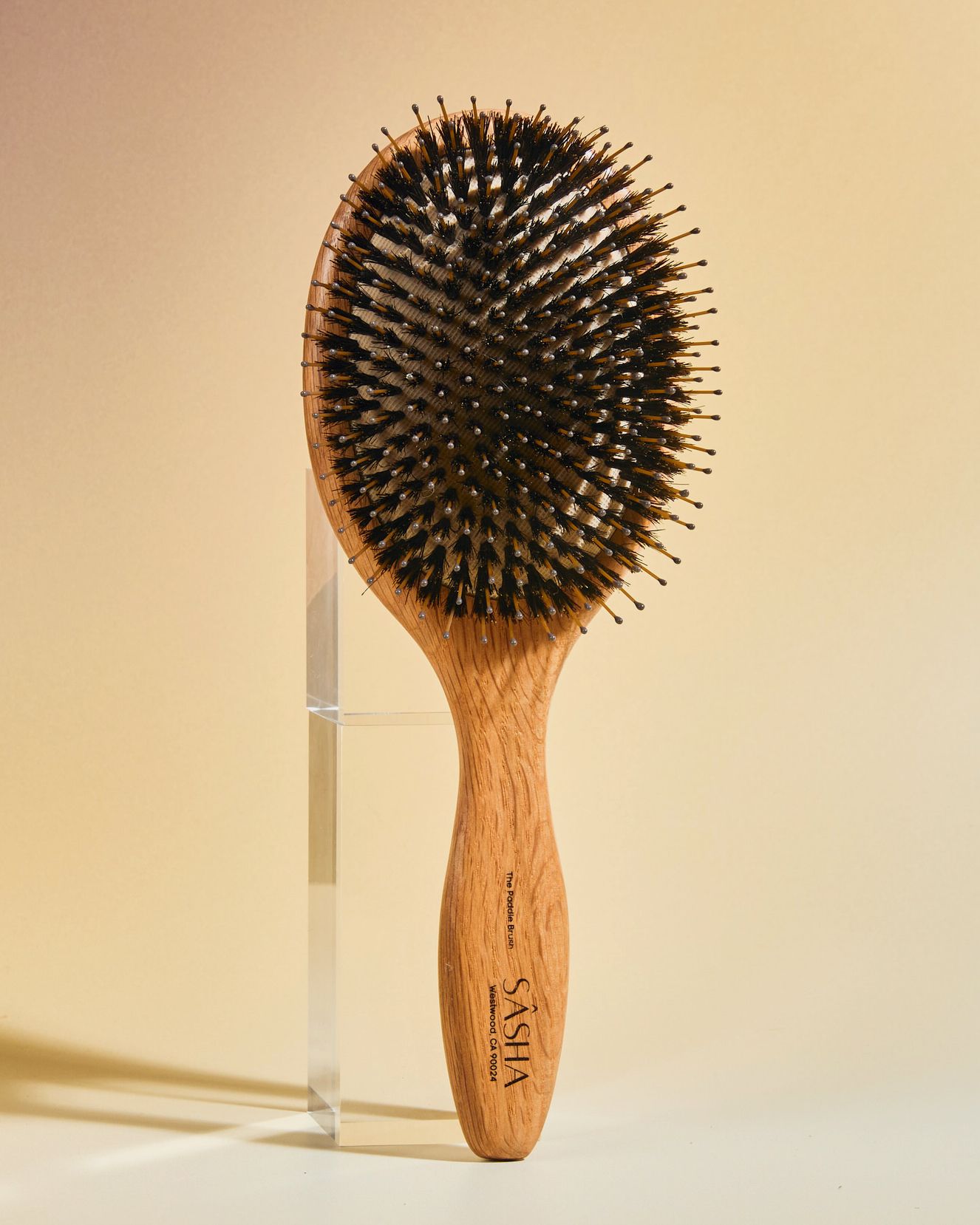 SASHA oval wooden paddle hair brush with boar bristles, displayed upright against a warm beige background.
