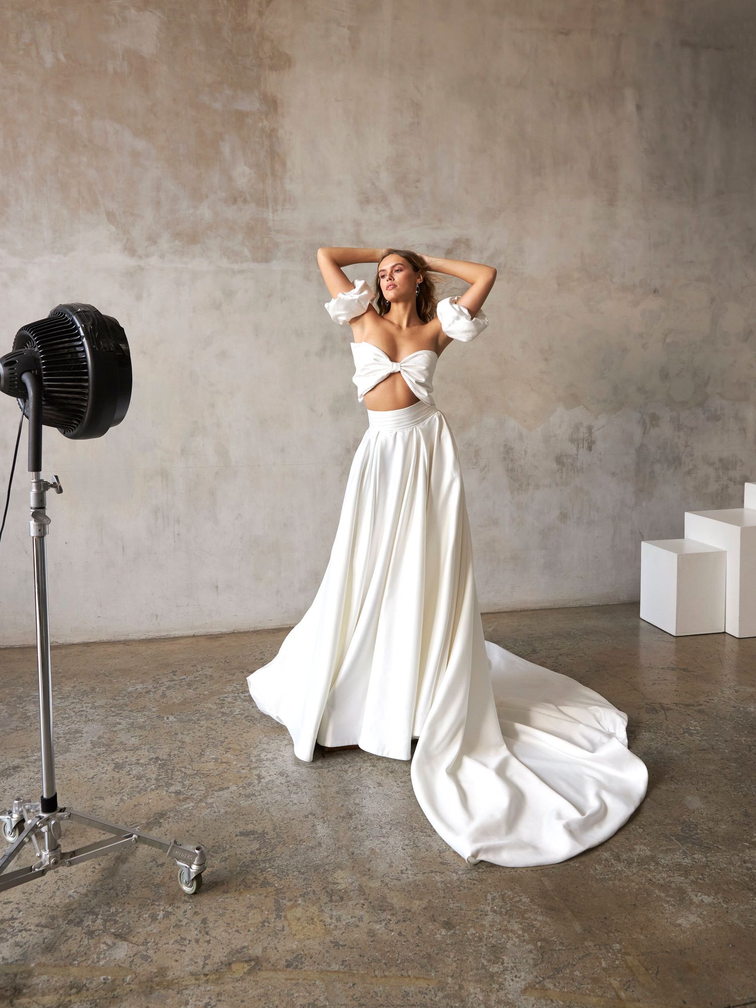 Elegant bridal two-piece set featuring an off-shoulder crop top and flowing white satin skirt with train in studio.