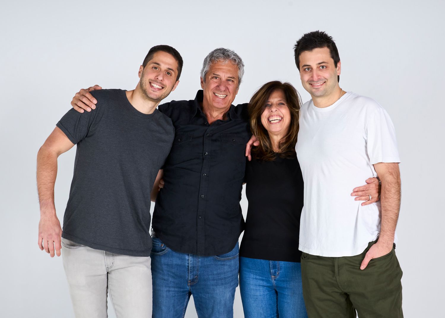 A happy family of four adults poses together smiling in a casual studio portrait session.