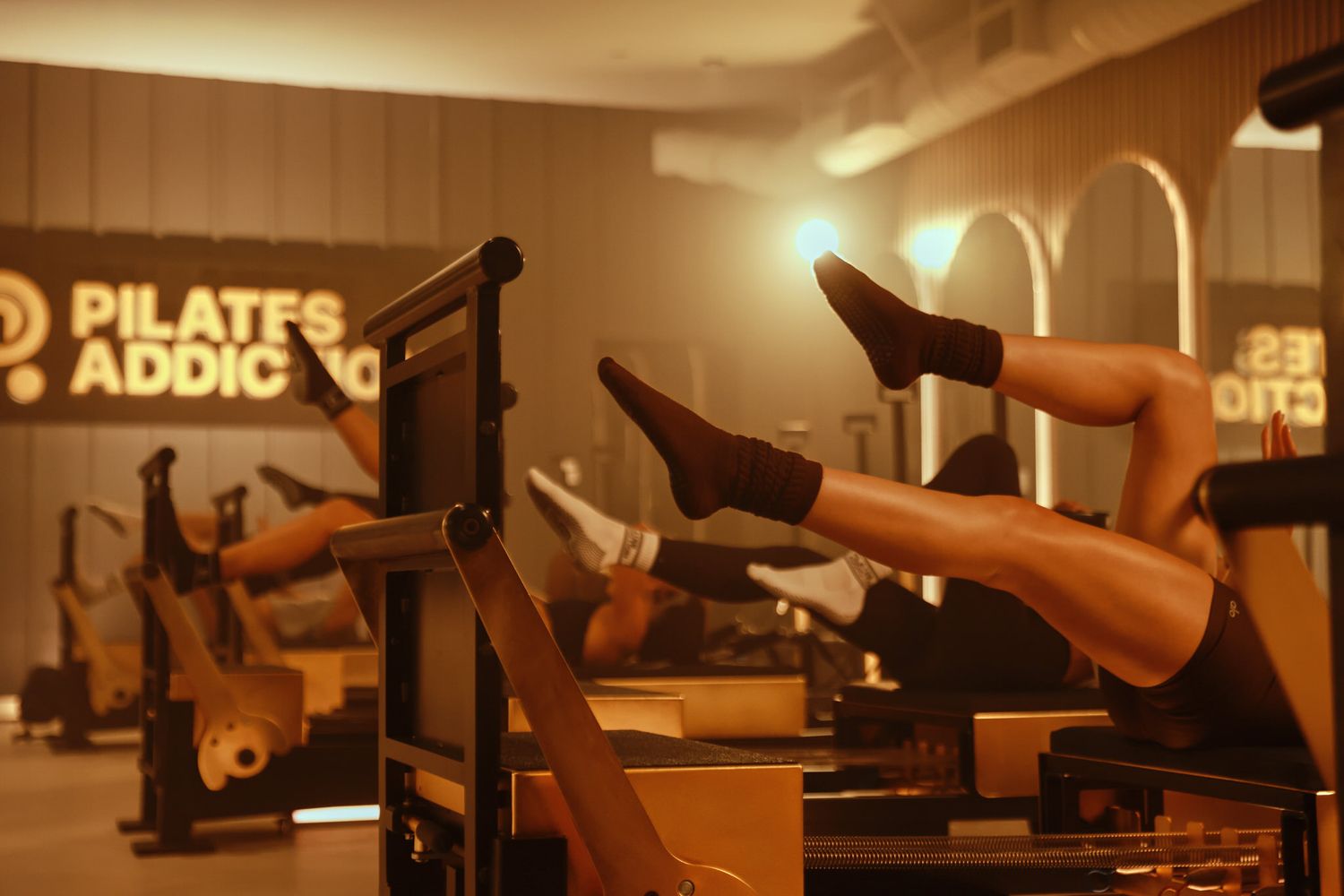 People doing Pilates reformer exercises with legs raised at Pilates Addicts studio.