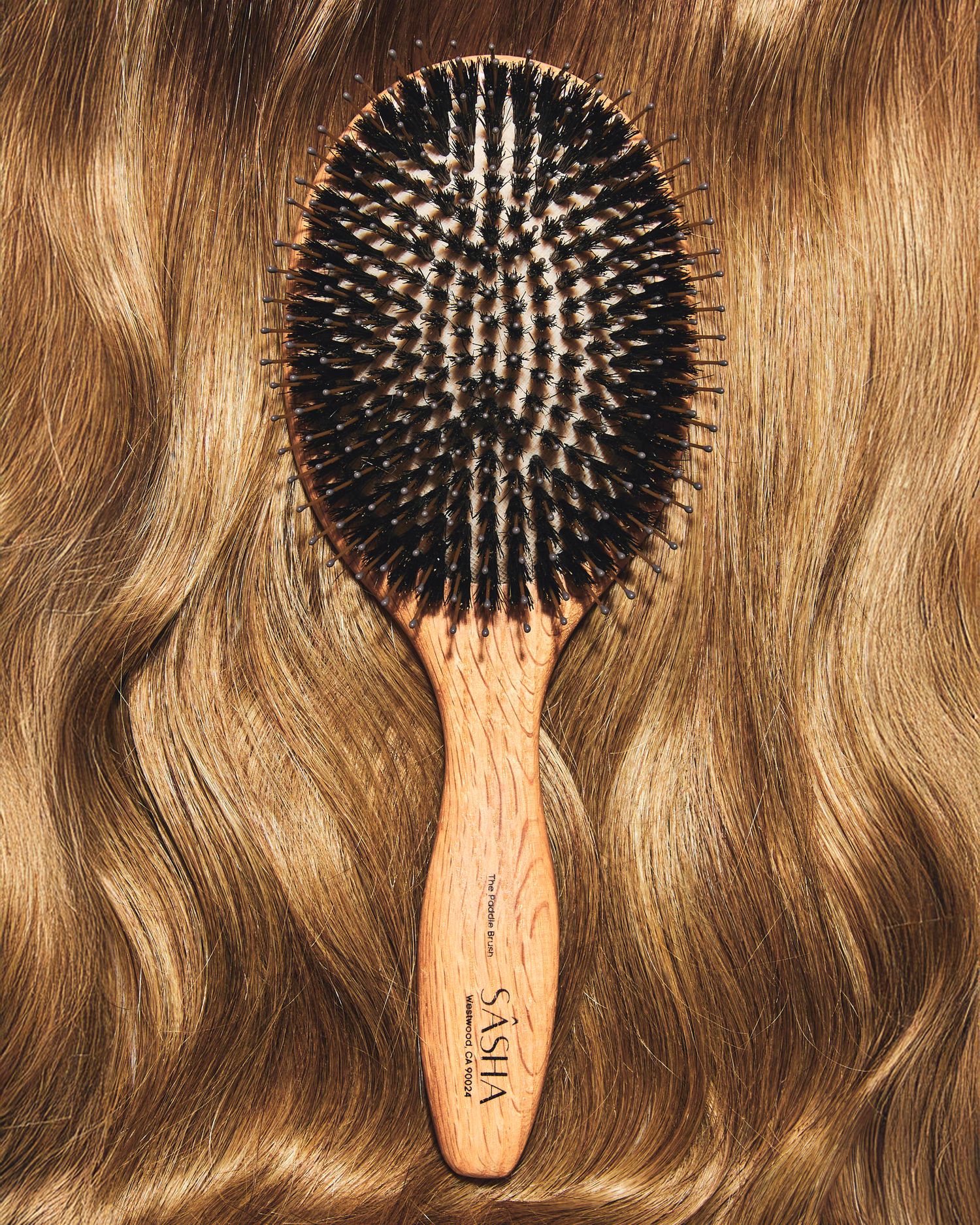 Vasha wooden oval hair brush with boar bristles resting on long wavy blonde highlighted hair.