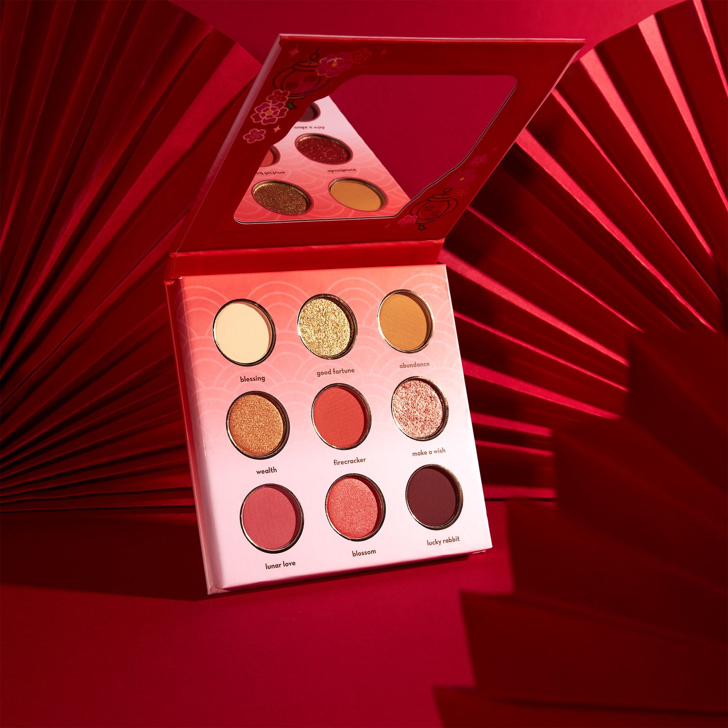 Luxurious red nine-pan eyeshadow palette with warm gold and red tones displayed on a bold red background.