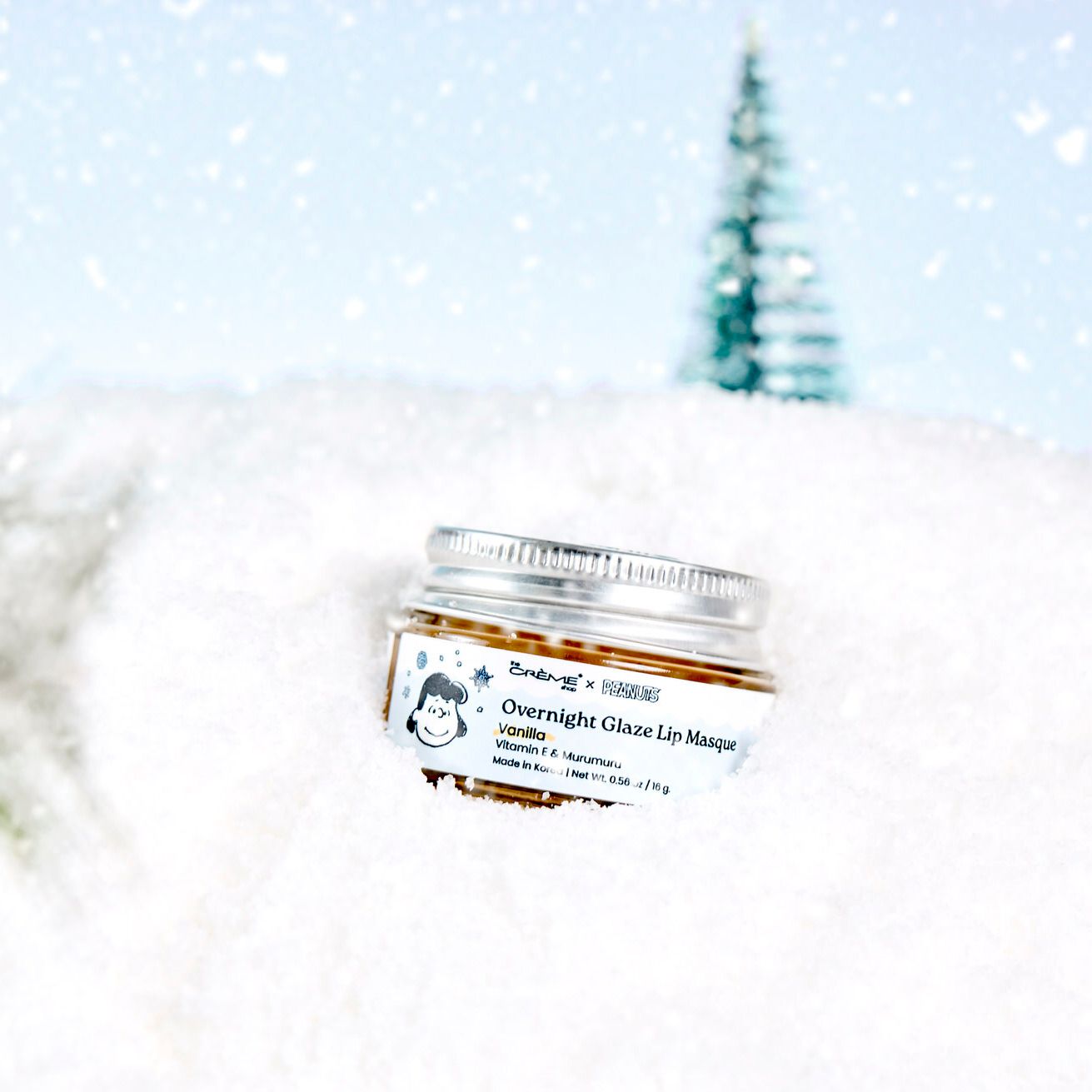 Overnight Glaze Lip Masque jar resting in snow with a snowy winter background and frosted pine tree.