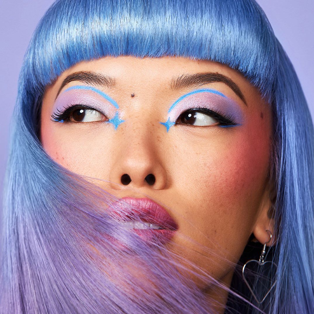 Model with blue straight hair and bangs wearing pastel purple eyeshadow with blue star eye art.