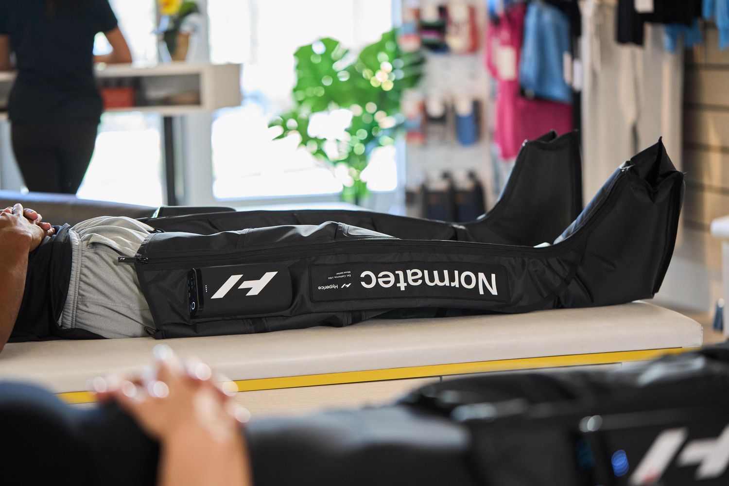 Person lying on a massage table wearing Normatec compression recovery boots in a sports therapy clinic.