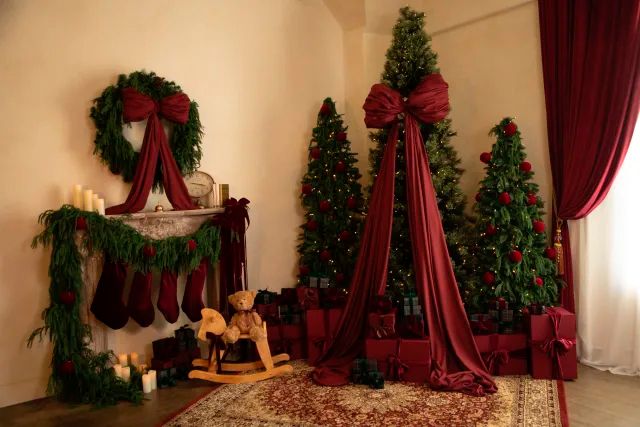 Festive Christmas room with decorated trees, red bows, stockings on mantle, candles, and wrapped gifts on a patterned rug.