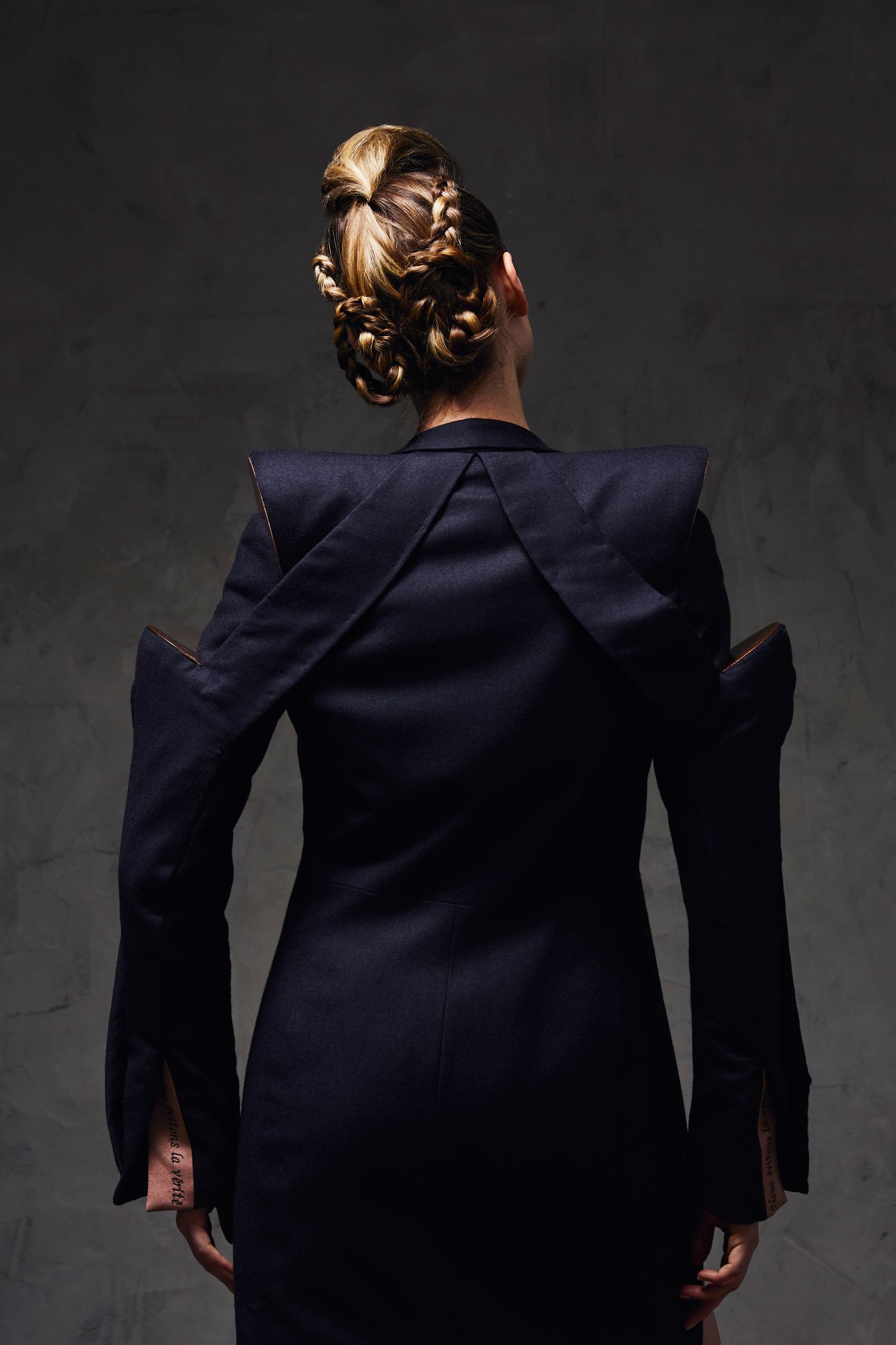 Back view of a woman in a structured navy blue avant-garde blazer dress with intricate braided updo hairstyle.