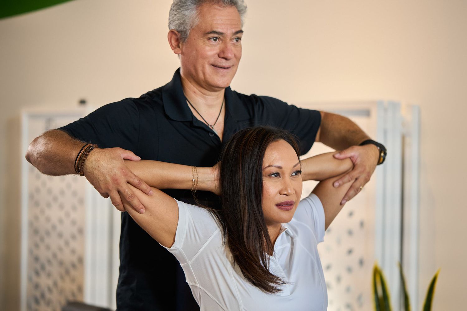 Trainer assisting woman with assisted shoulder and arm stretch therapy.