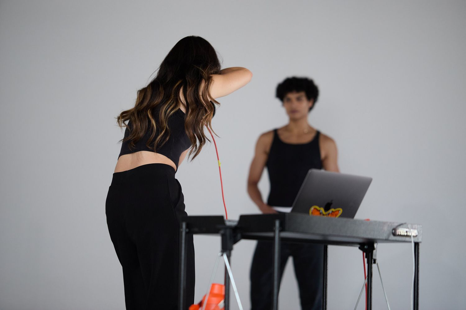 Two people in a photography studio, one using a laptop at a treadmill desk while another stretches nearby.