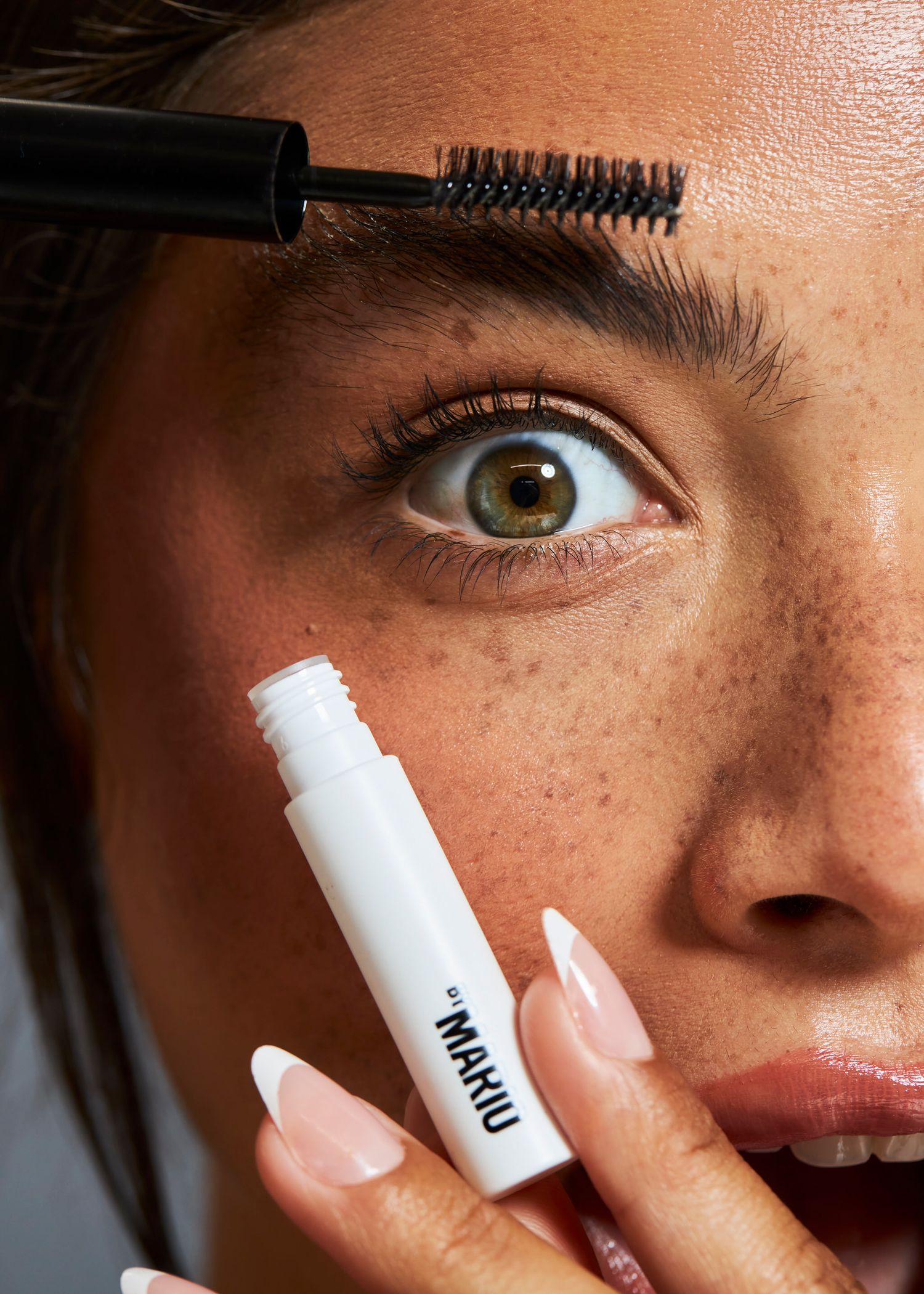 Close-up of a woman applying NAHU brow gel with a spoolie brush to her well-groomed eyebrows.