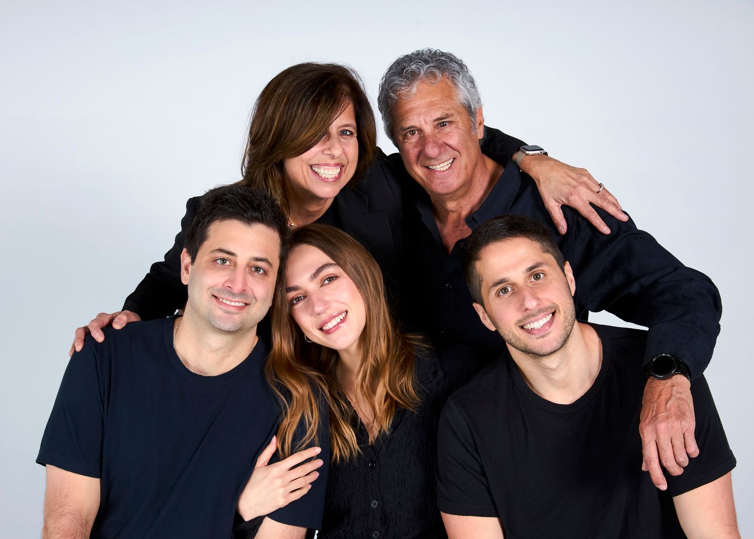 A joyful family of five smiles together in matching black outfits during a studio portrait session.