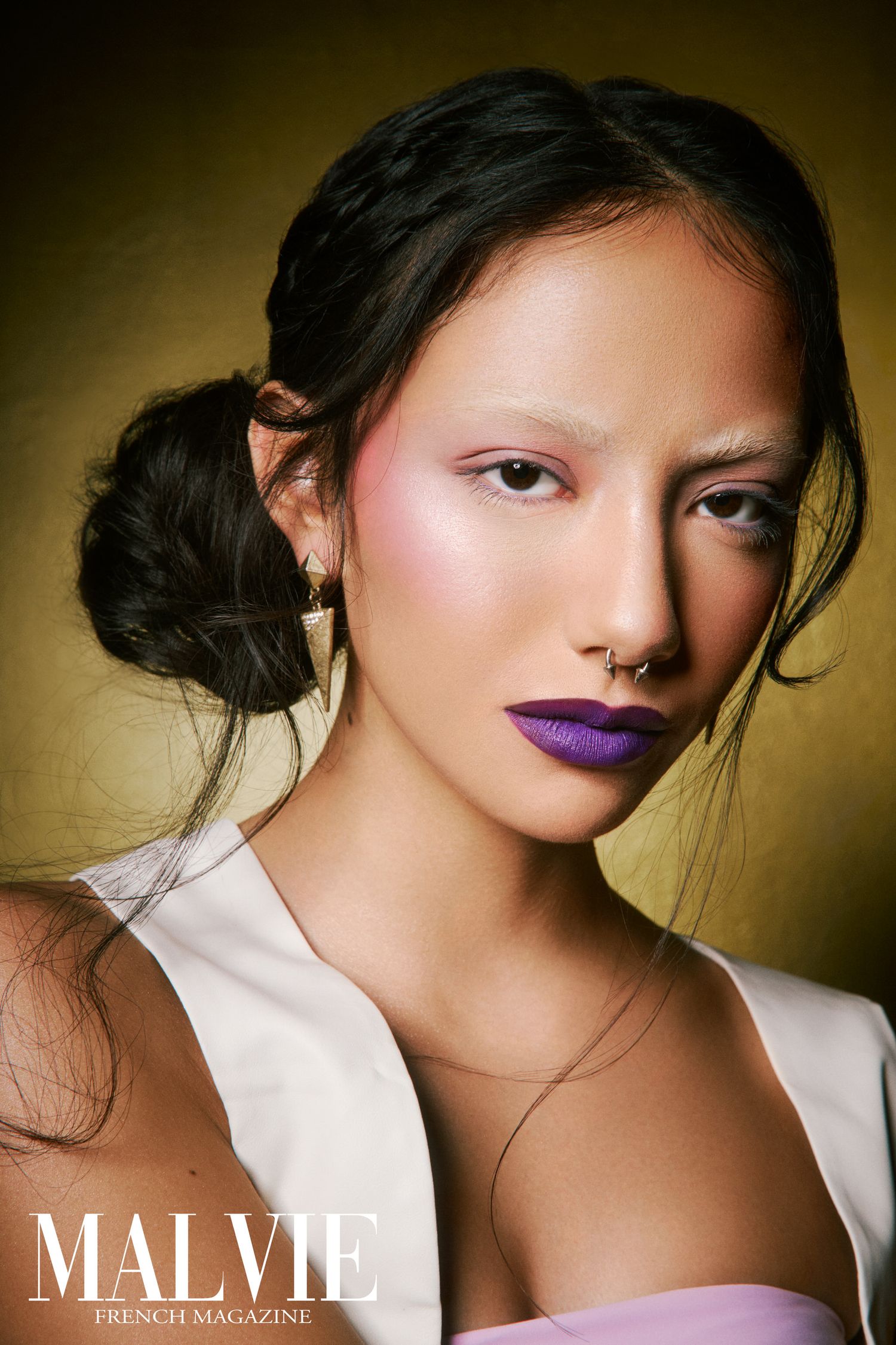Woman with purple lipstick, pink eye makeup, nose ring, and updo hairstyle in Malvie French Magazine portrait.