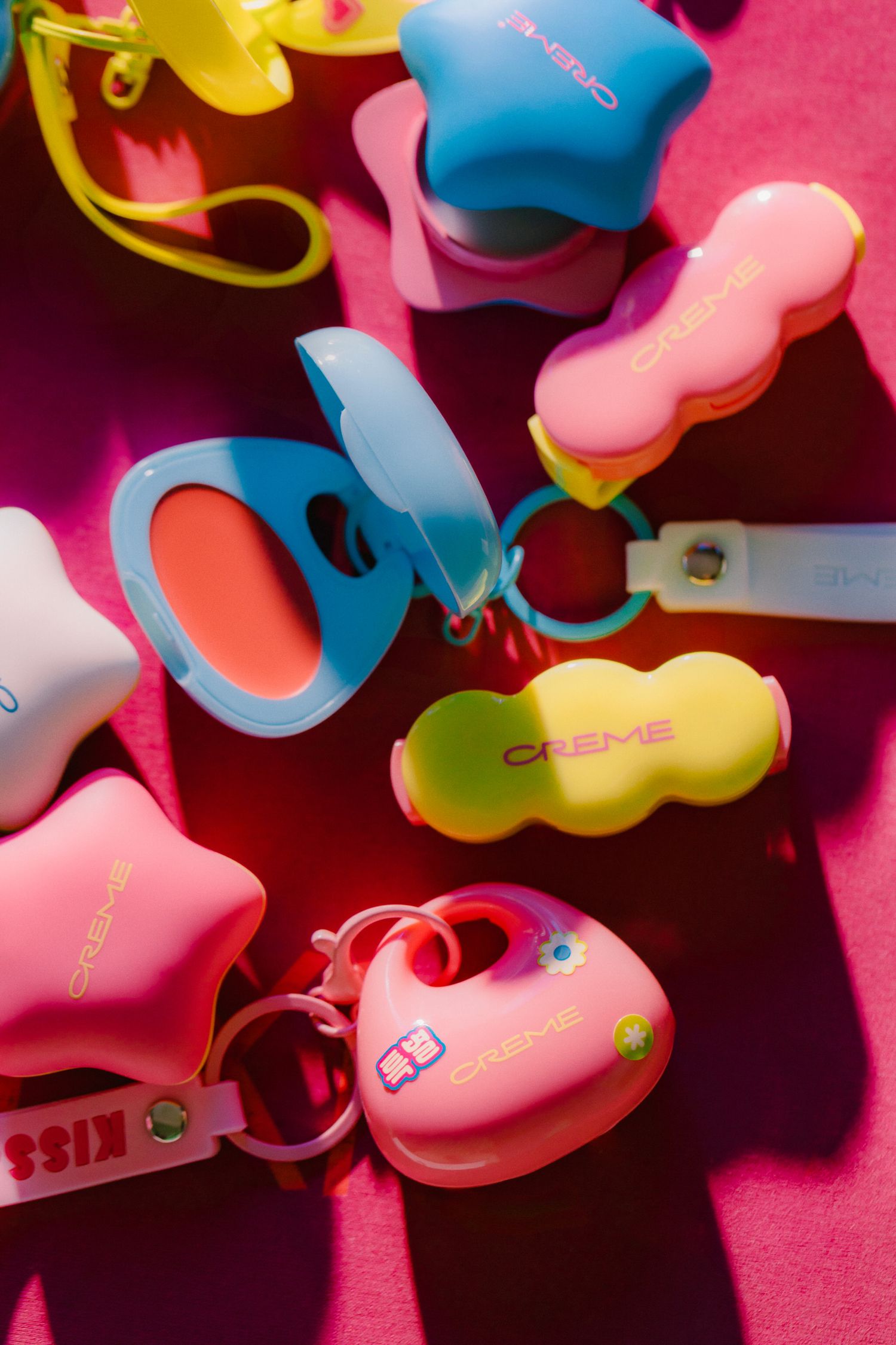 Colorful product shot of Creme brand in pink, blue, and yellow scattered on a pink surface by LA beauty photographer Belva Chan.