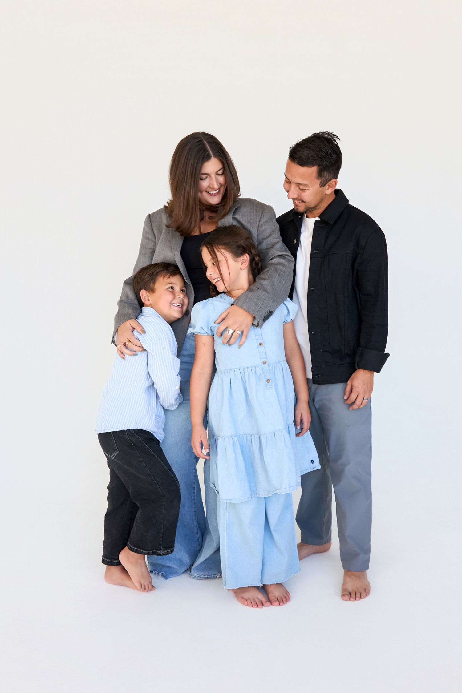 Happy family of four posing together in a white studio, parents embracing children in casual blue and black outfits.