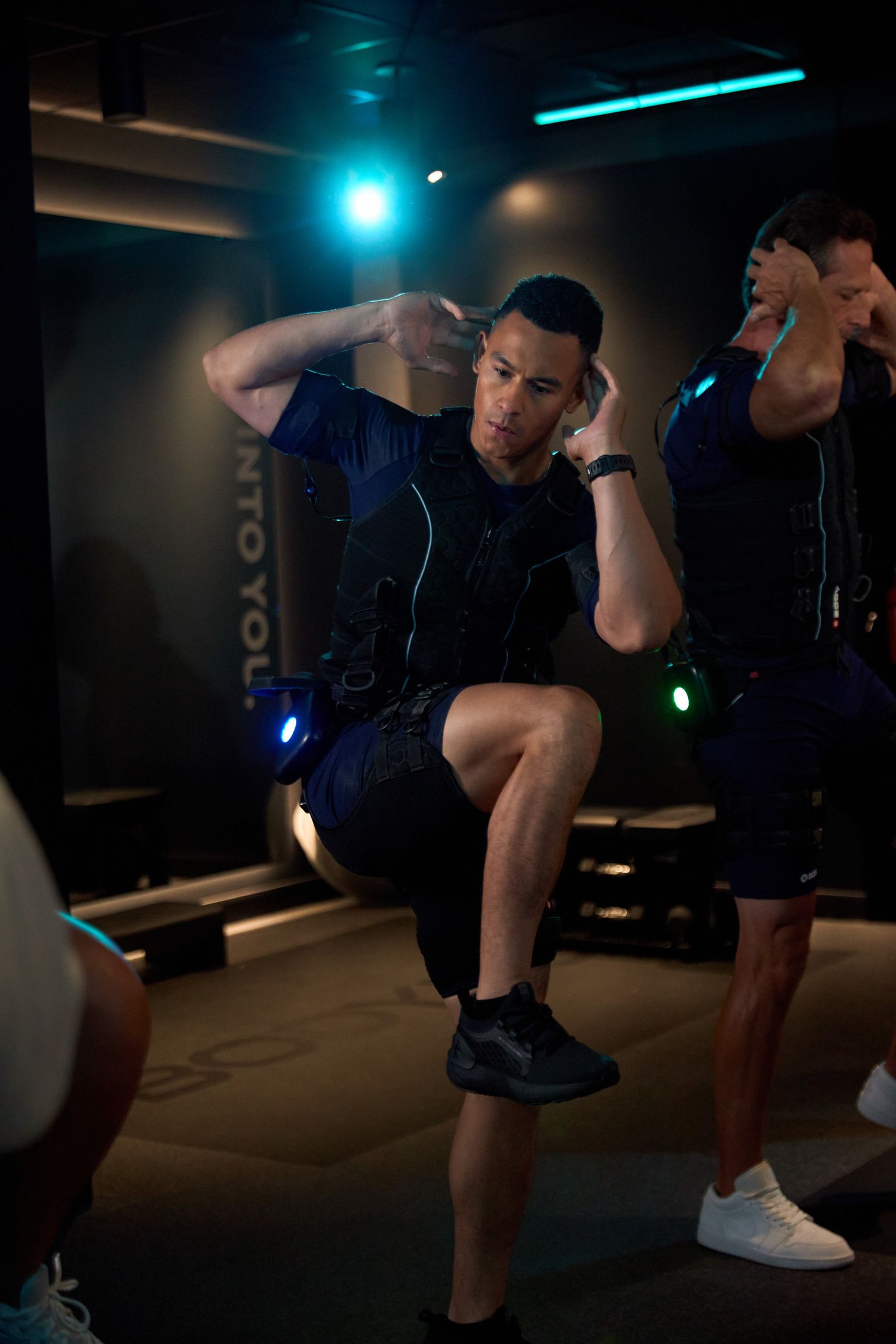 Men wearing EMS training suits perform high-knee exercises during an electro muscle stimulation workout session.