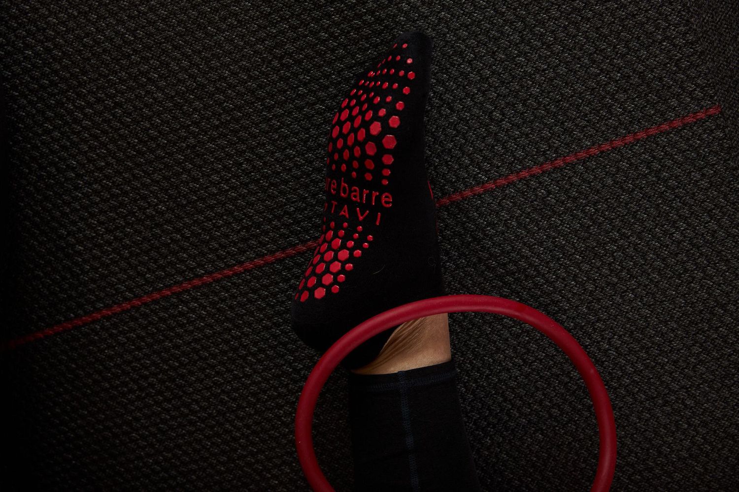 Top-down view of a Pure Barre grip sock and resistance ring on a dark textured floor.