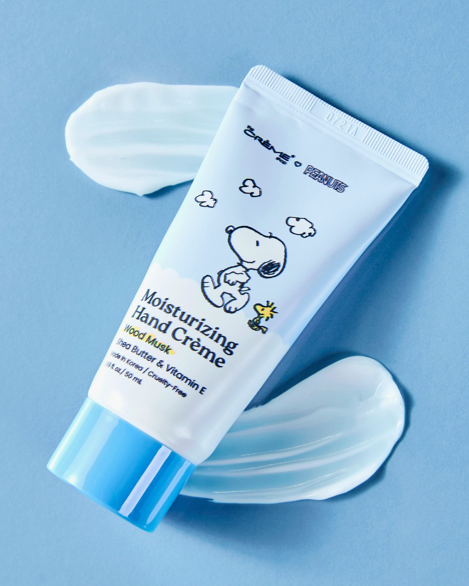 Snoopy Moisturizing Hand Creme tube with shea butter and Vitamin E on a blue background with cream swatches.
