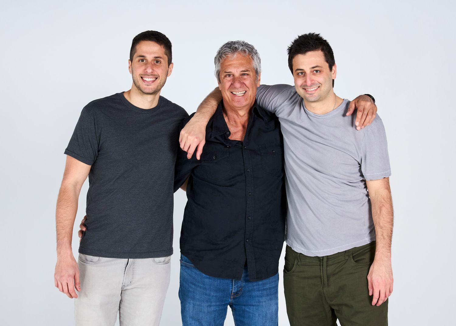 Three smiling men posing together with arms around each other against white studio background.