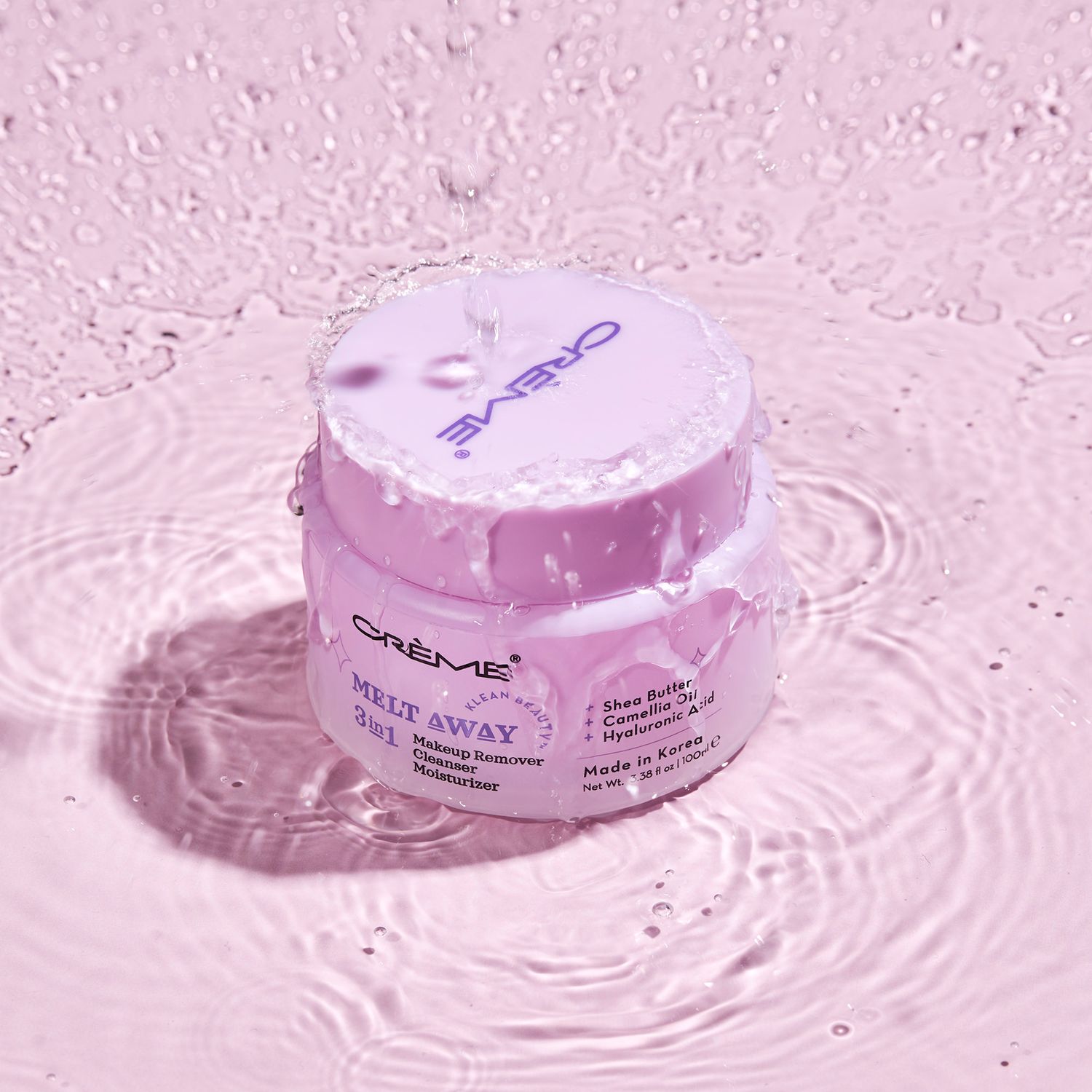 Crème Melt Away gel cleansing balm jar with shea butter and cornflower, splashing in water on pink background.