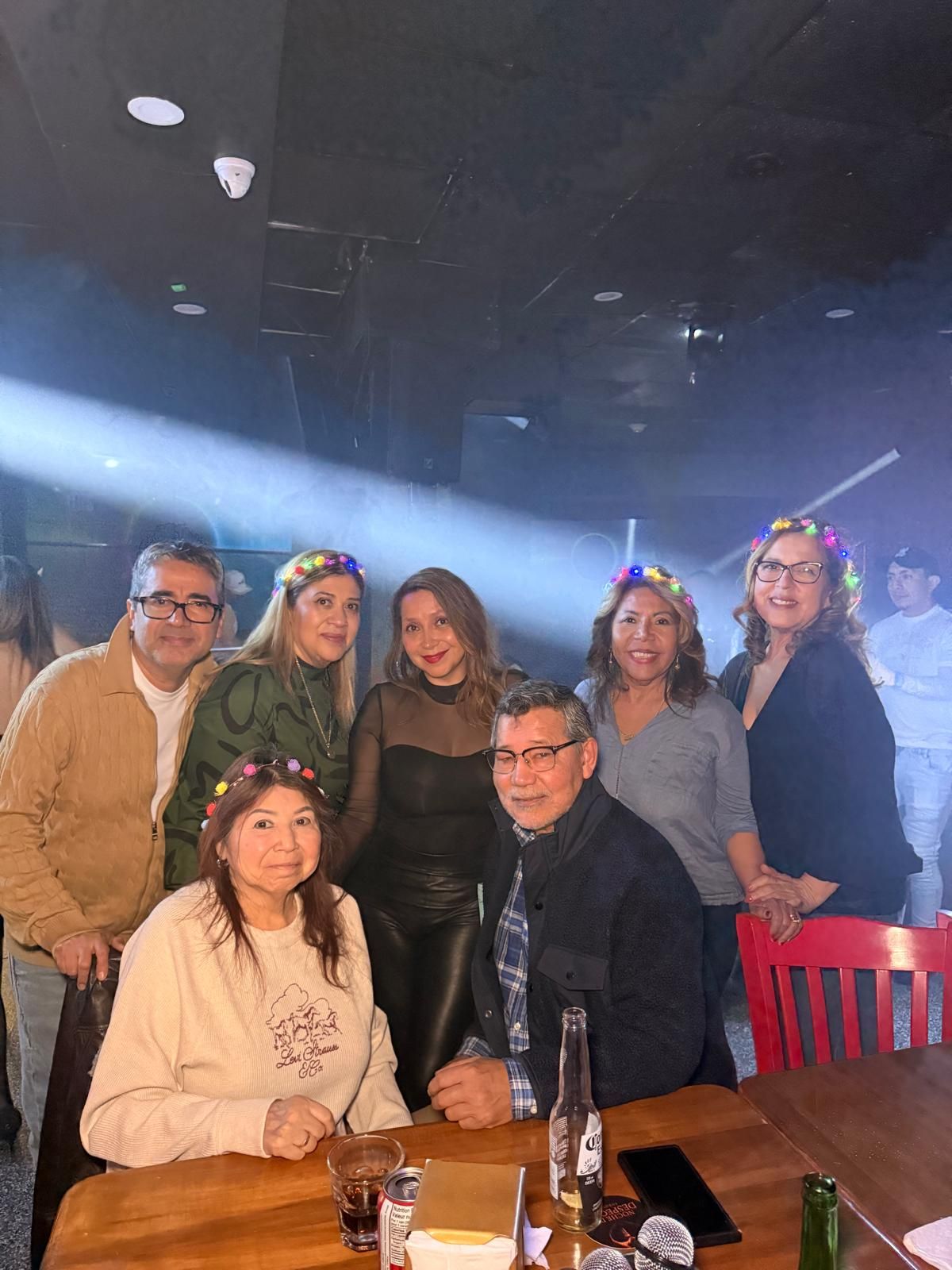 A group of people gathered at a dimly lit venue with blue lighting enjoying drinks and socializing at tables.