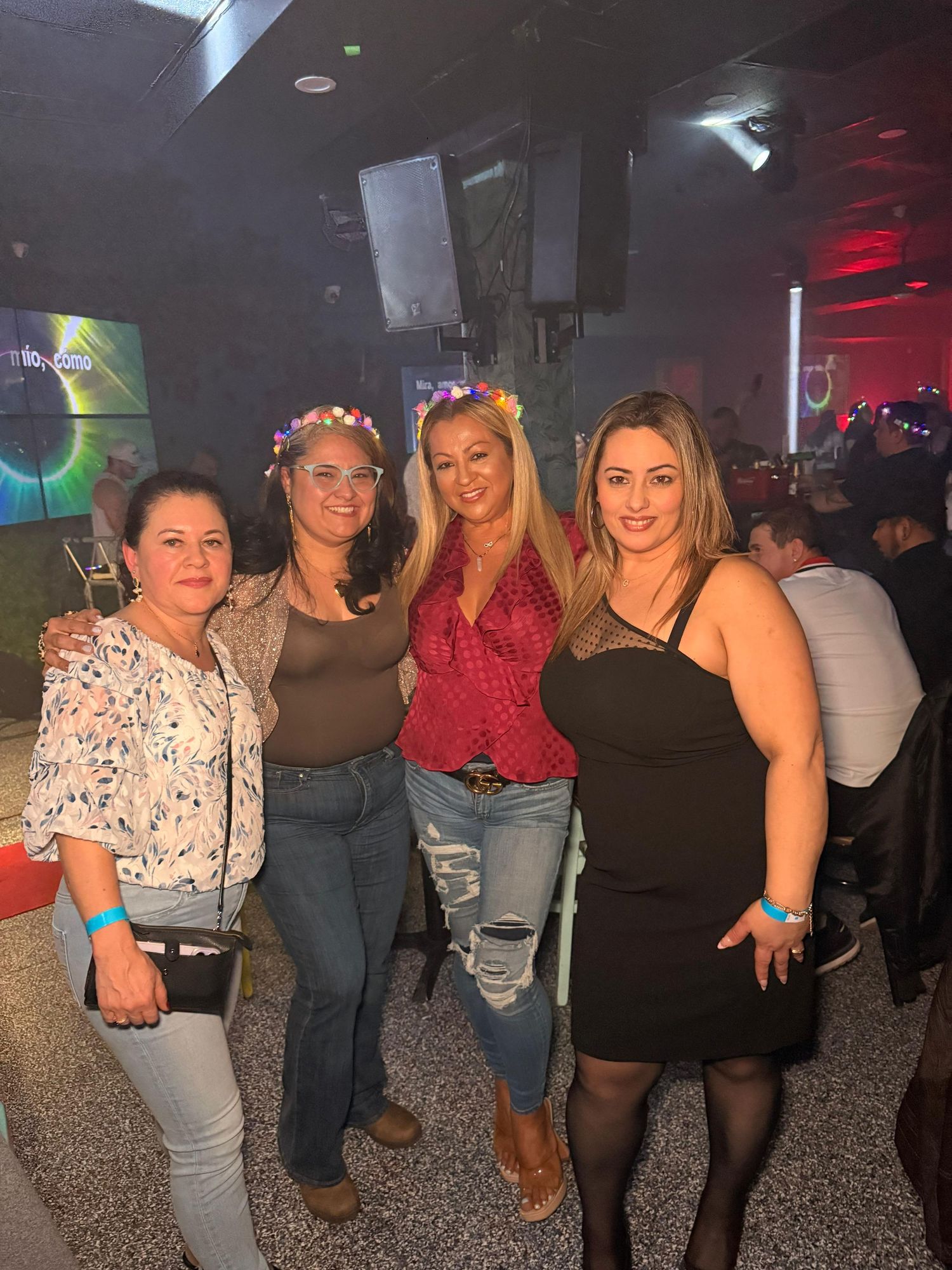 Four friends pose together at a nightclub with colorful lighting and decorative elements.